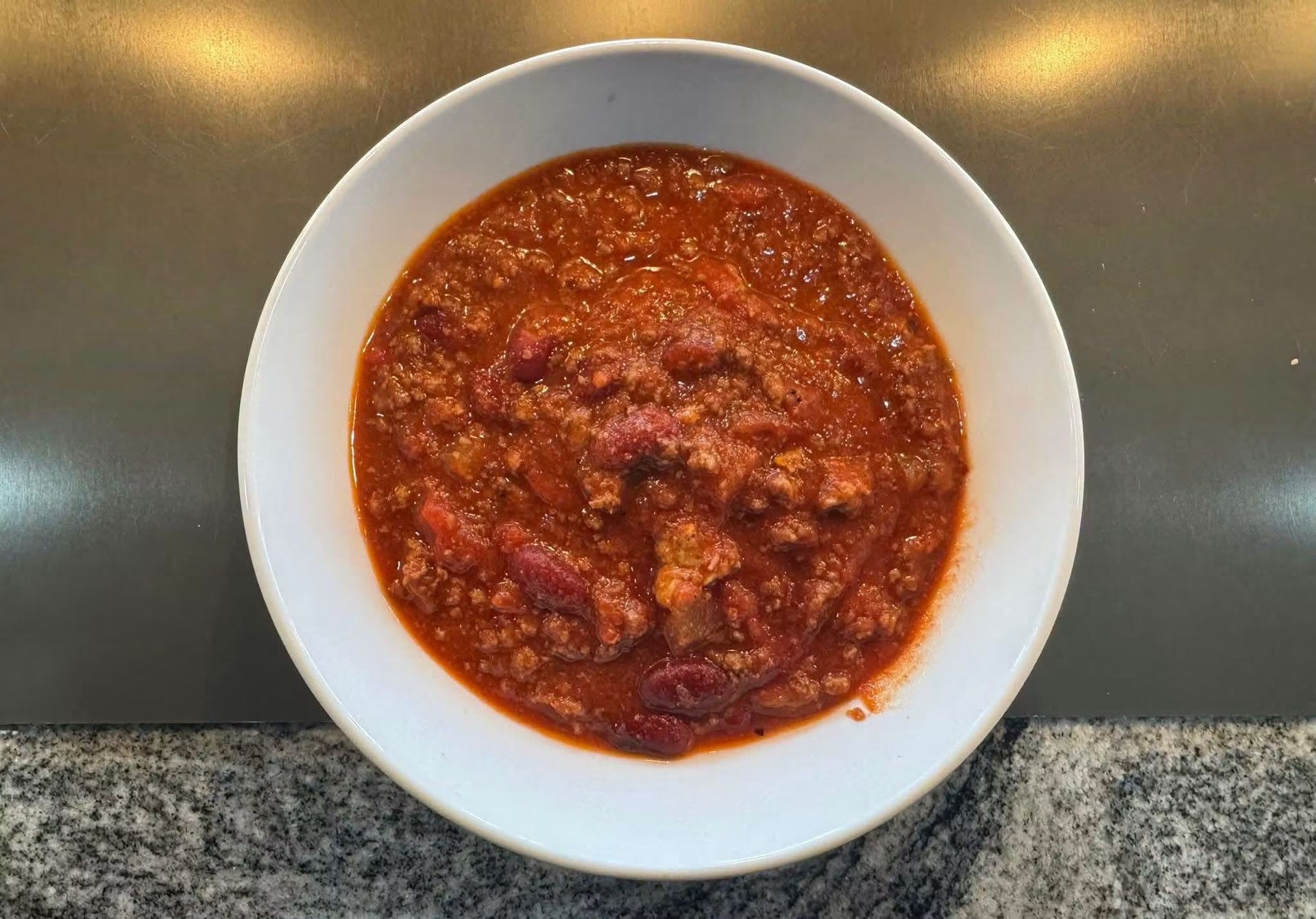 White bowl of red chunky soup or stew on a countertop, viewed from above.