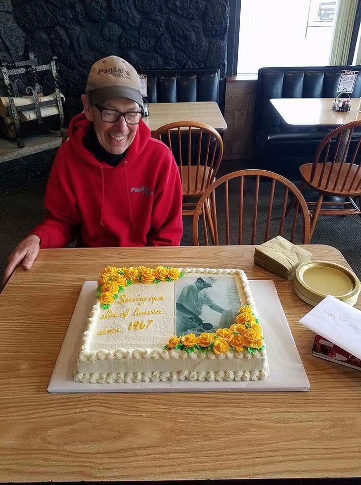 Person in red jacket smiles beside a decorated cake on a restaurant table.
