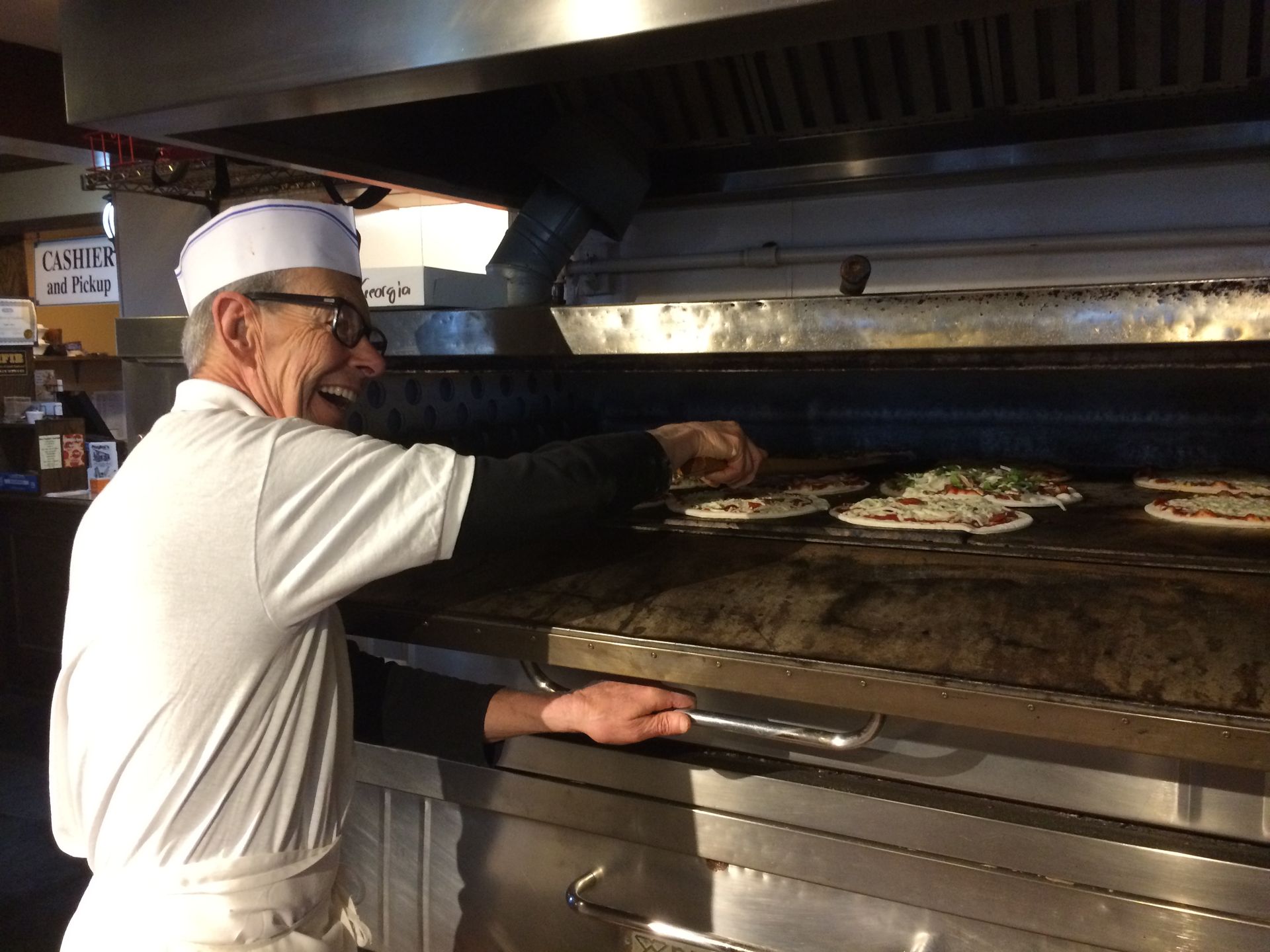 Chef sliding pizza into a wood-fired oven in a restaurant kitchen