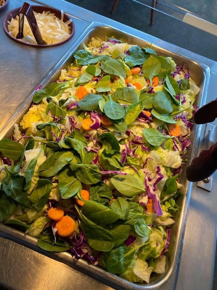 Fresh salad bar with mixed greens, purple cabbage, orange carrots, and tongs in a metal tray