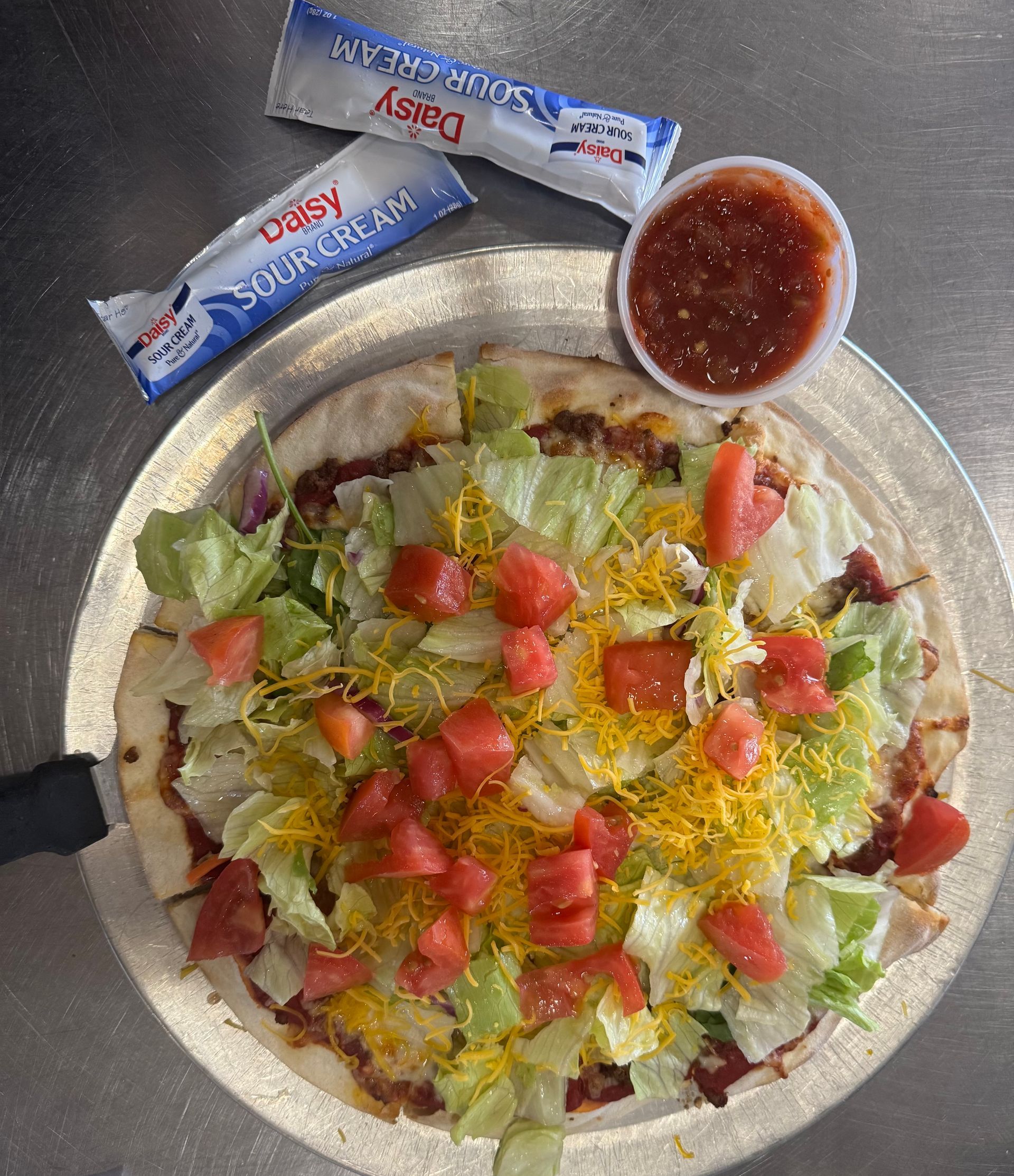 Taco salad with lettuce, tomatoes, cheese, and tortilla strips, plus two condiment packets and salsa cup.