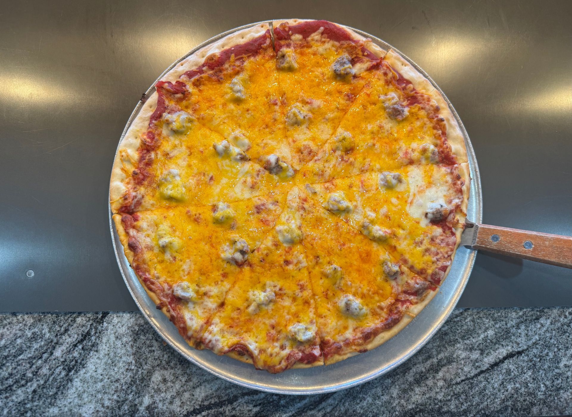 Baked cheese pizza in a round pan with a metal handle on a dark countertop.