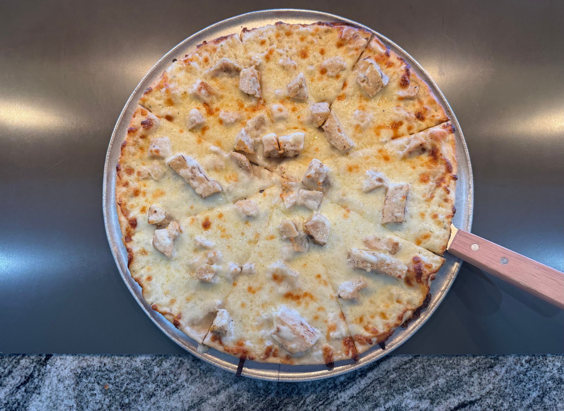 Cheese-topped pizza in a round pan with a slice serving spatula on a countertop