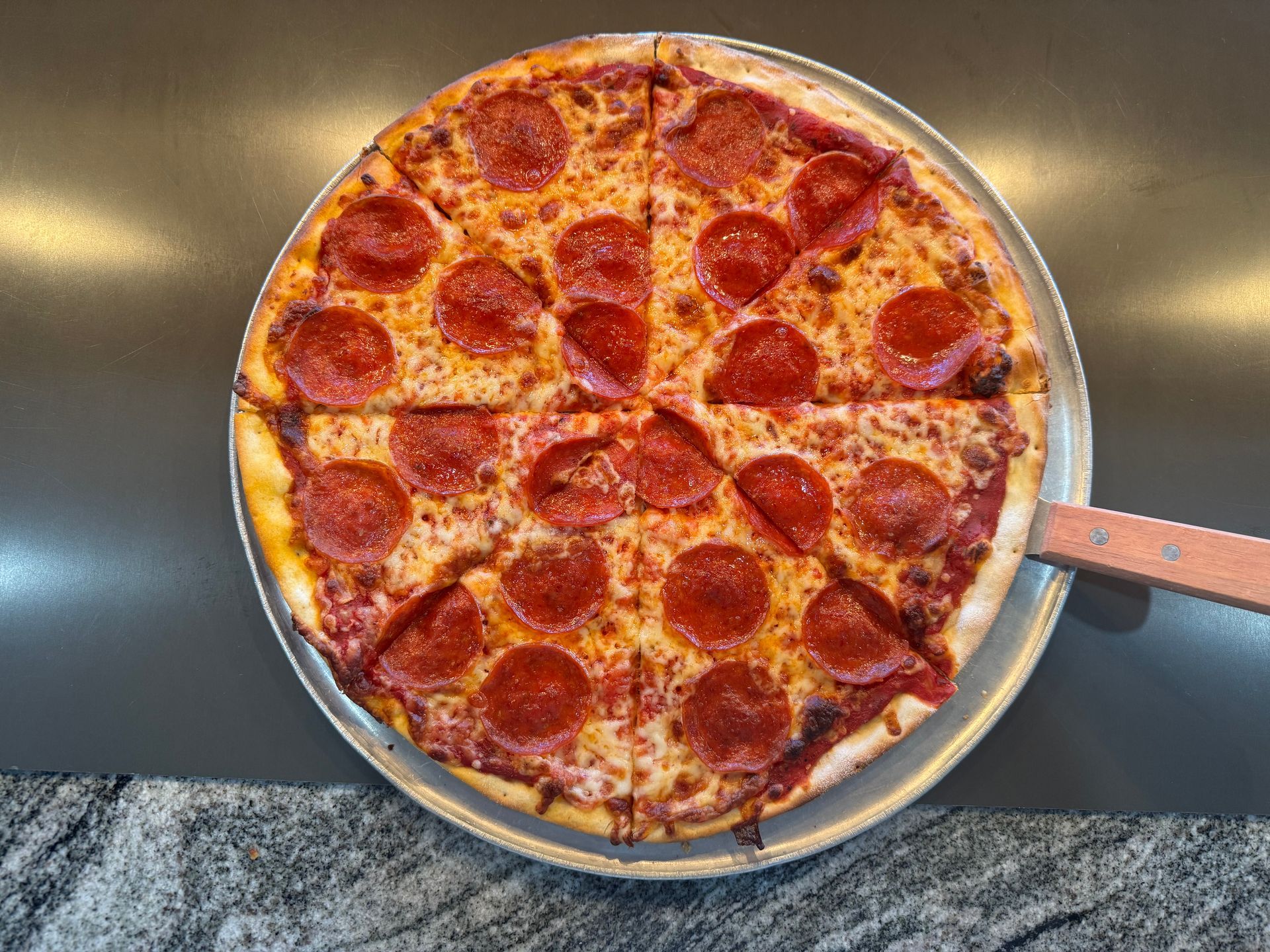 Pepperoni pizza in a pan, viewed from above, with a slice missing and a metal handle on the right