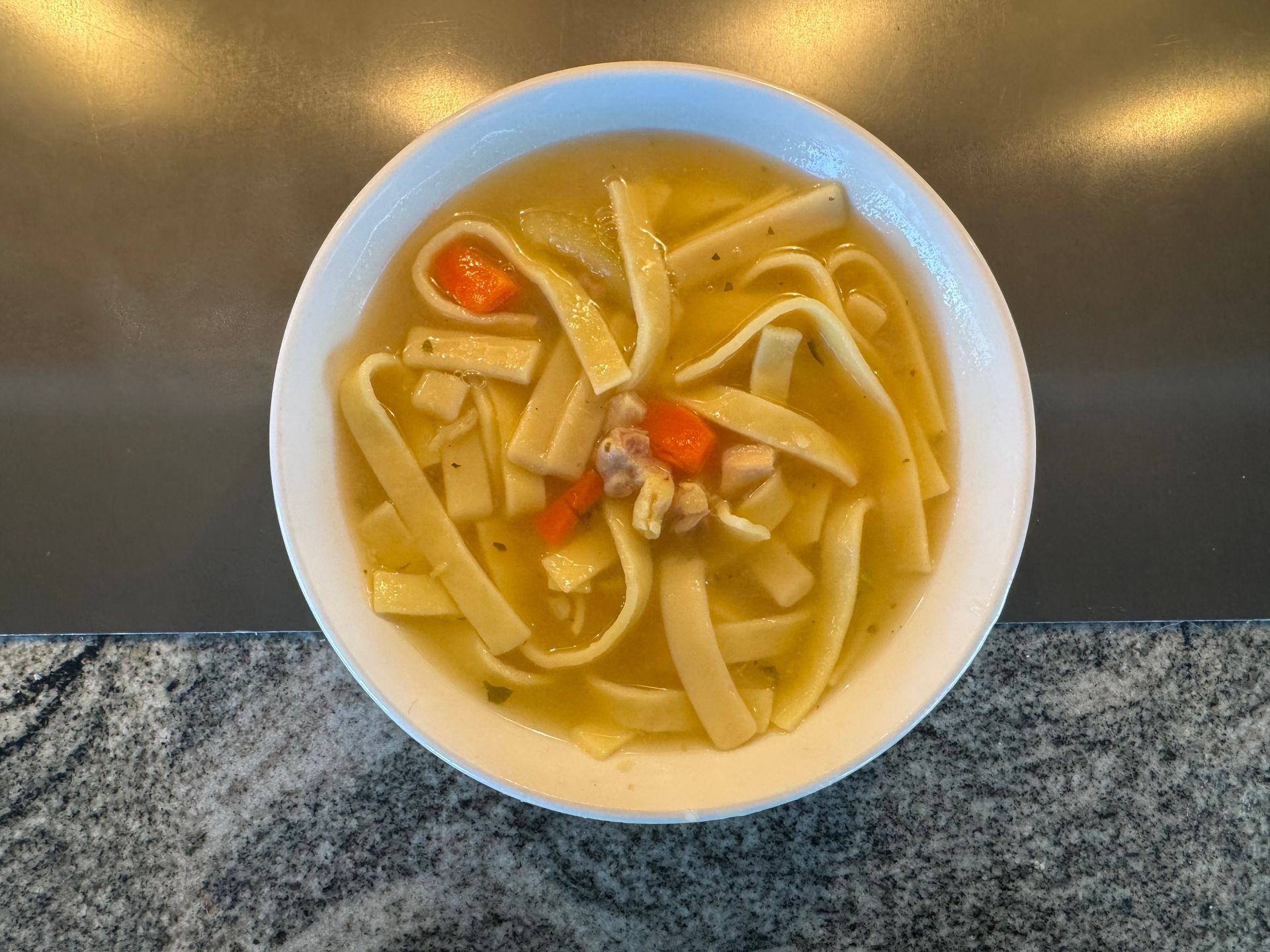 Bowl of noodle soup with vegetables on a stainless steel table.
