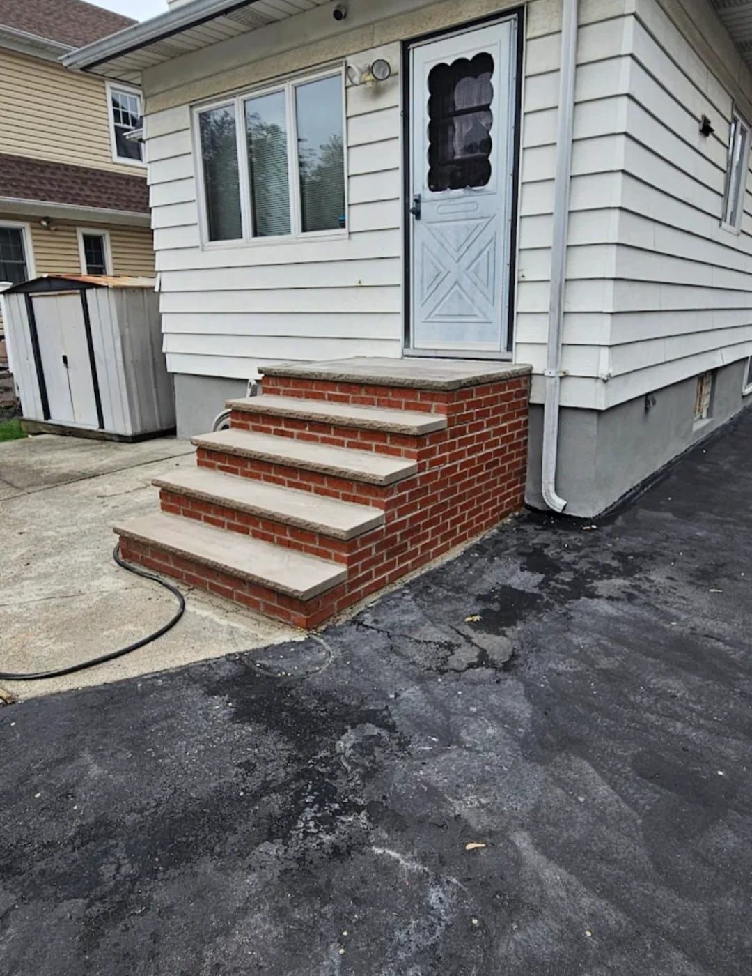 Brick steps leading to a white door of a house with white siding and gray asphalt driveway.