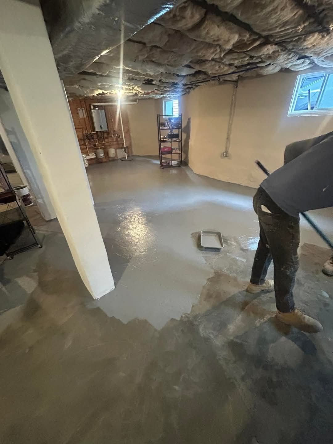 Person applying a gray coating to a concrete basement floor.