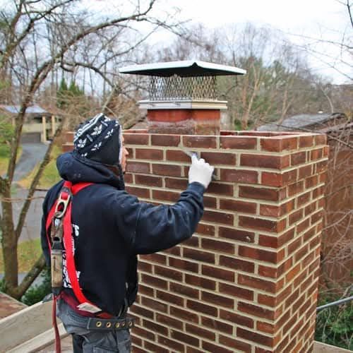 Person on rooftop repairing brick chimney. Safety harness visible.