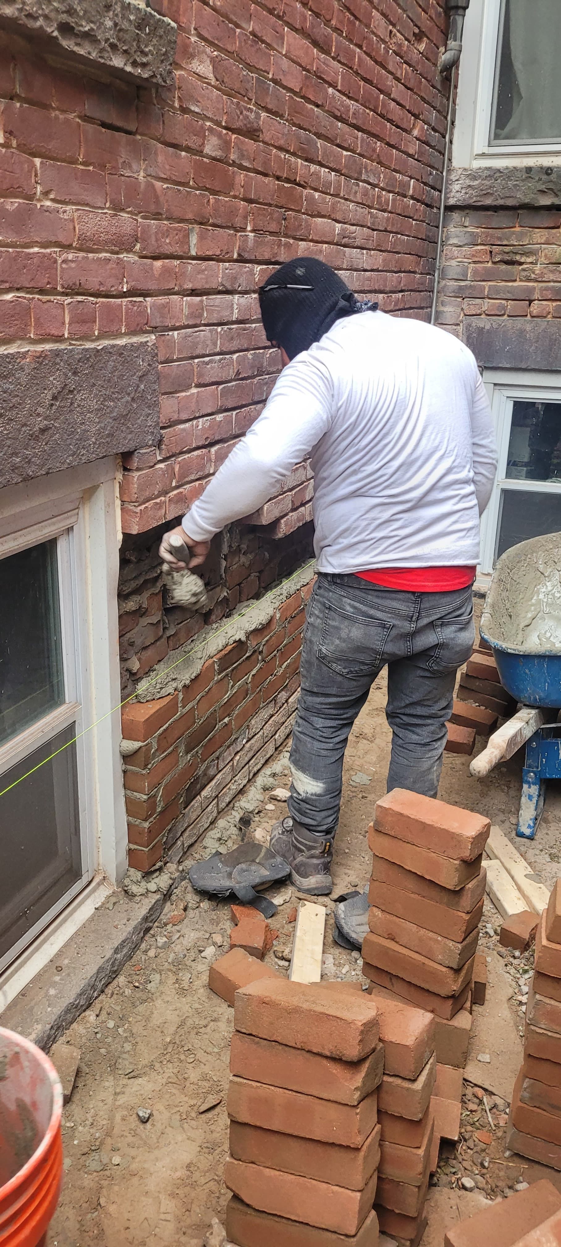 A person in a black cap laying bricks on a building. Bricks stacked nearby.