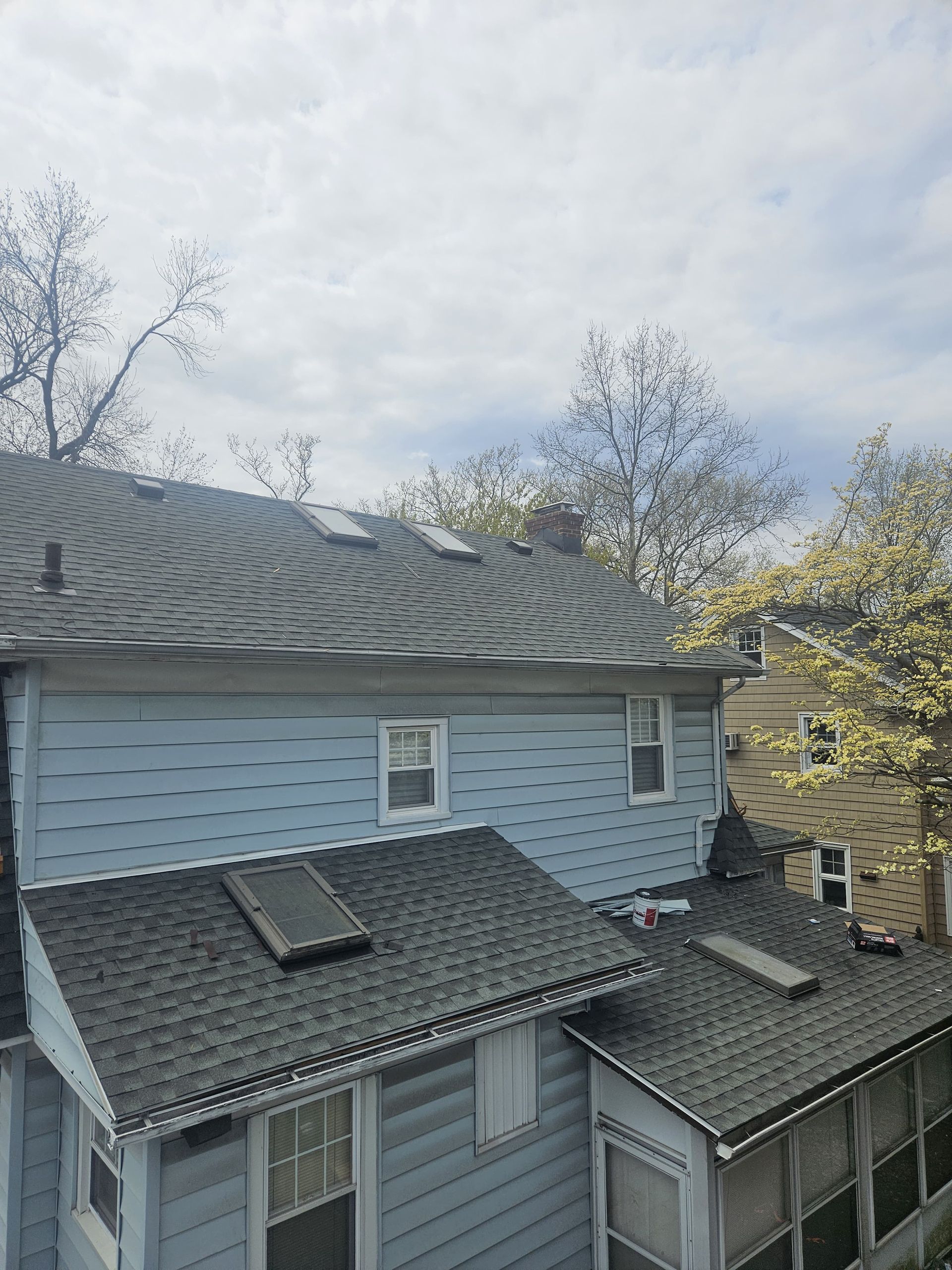 Blue house with multiple roof levels, skylights, and a cloudy sky.