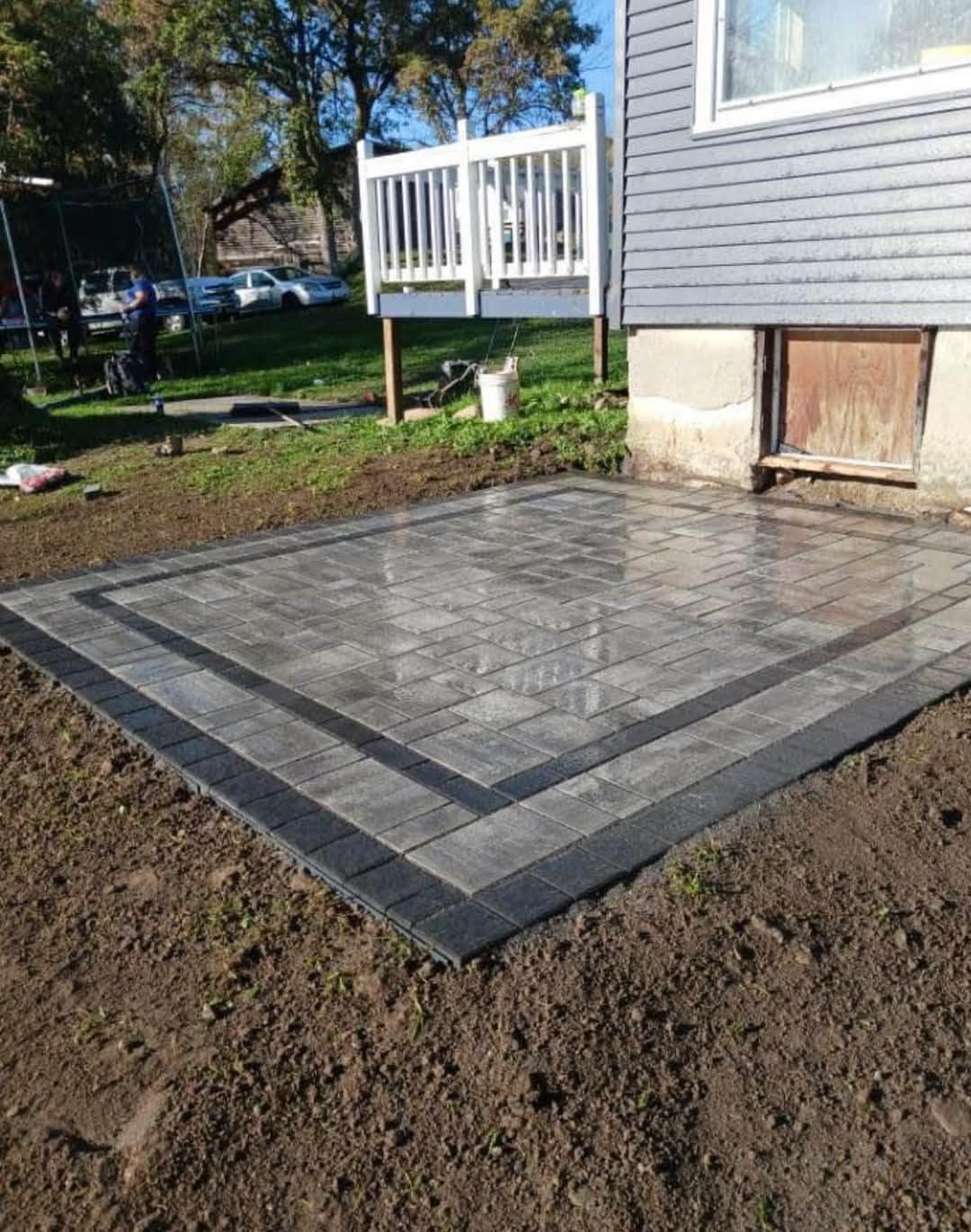 Newly constructed gray brick patio with black border, next to a house.