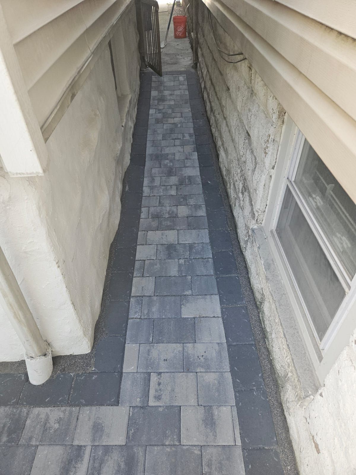 Narrow walkway paved with dark gray rectangular tiles between two building walls.