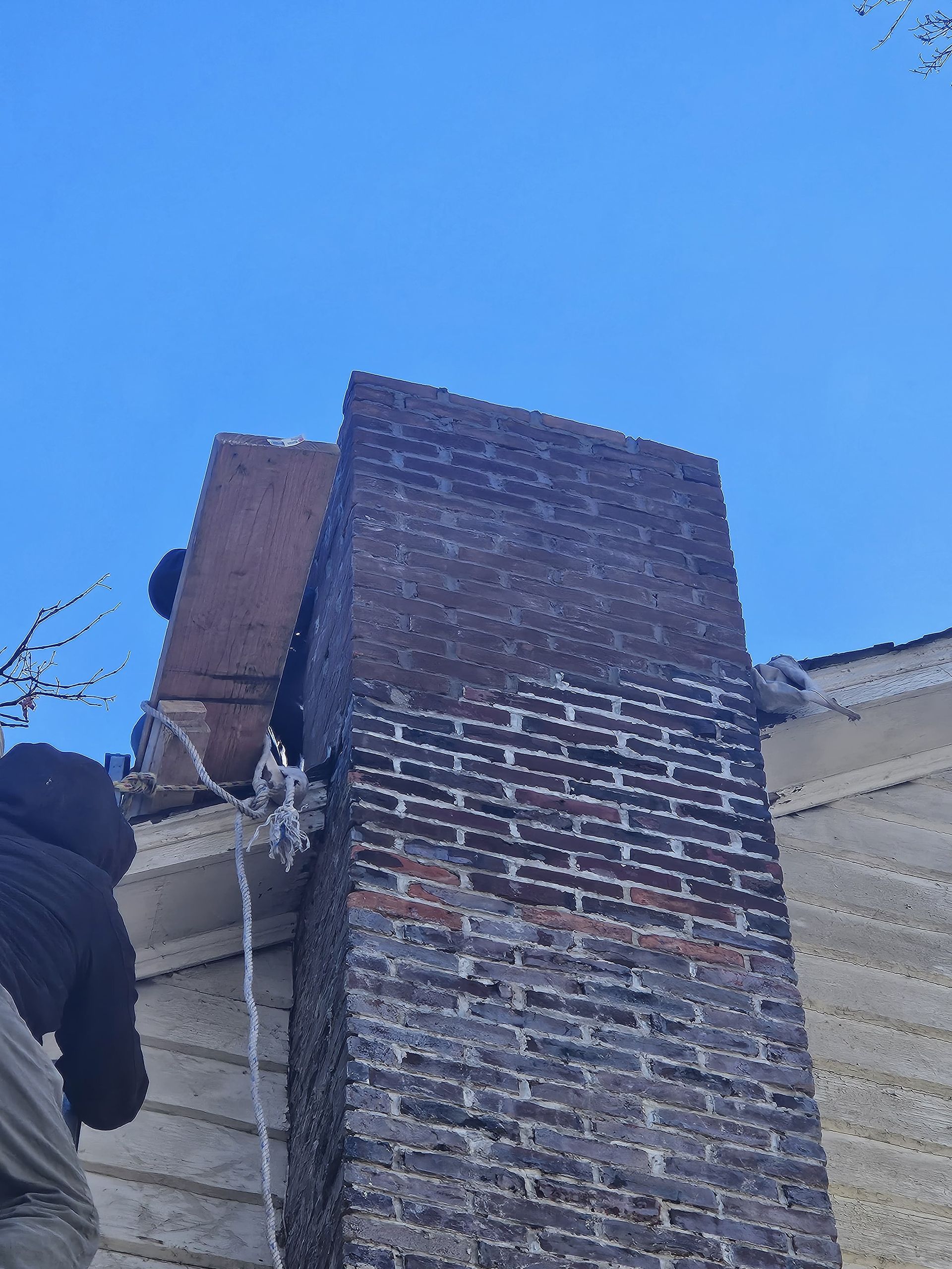 A person working on a brick chimney against a blue sky.