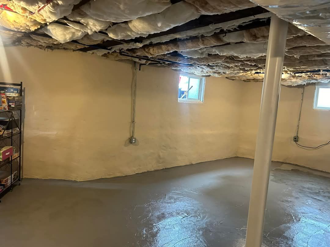 Basement with light-colored walls, gray floor, insulation on ceiling, a support beam, and small windows.
