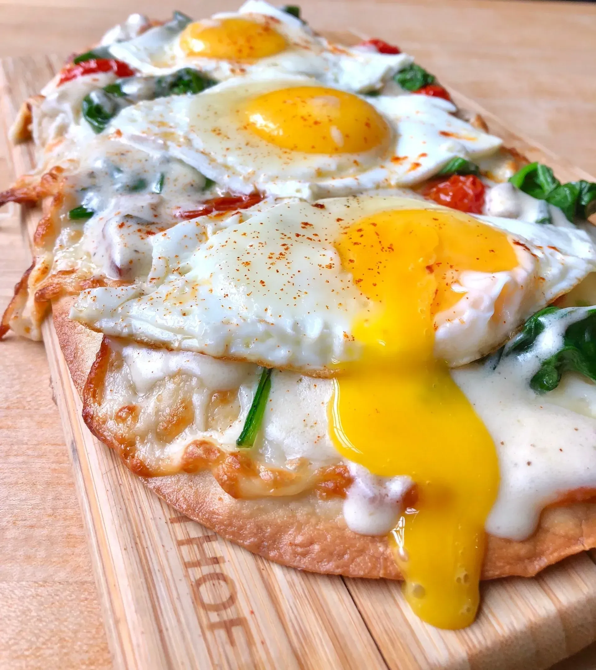Three-egg pizza with melted cheese, herbs, and a runny yolk on a wooden board