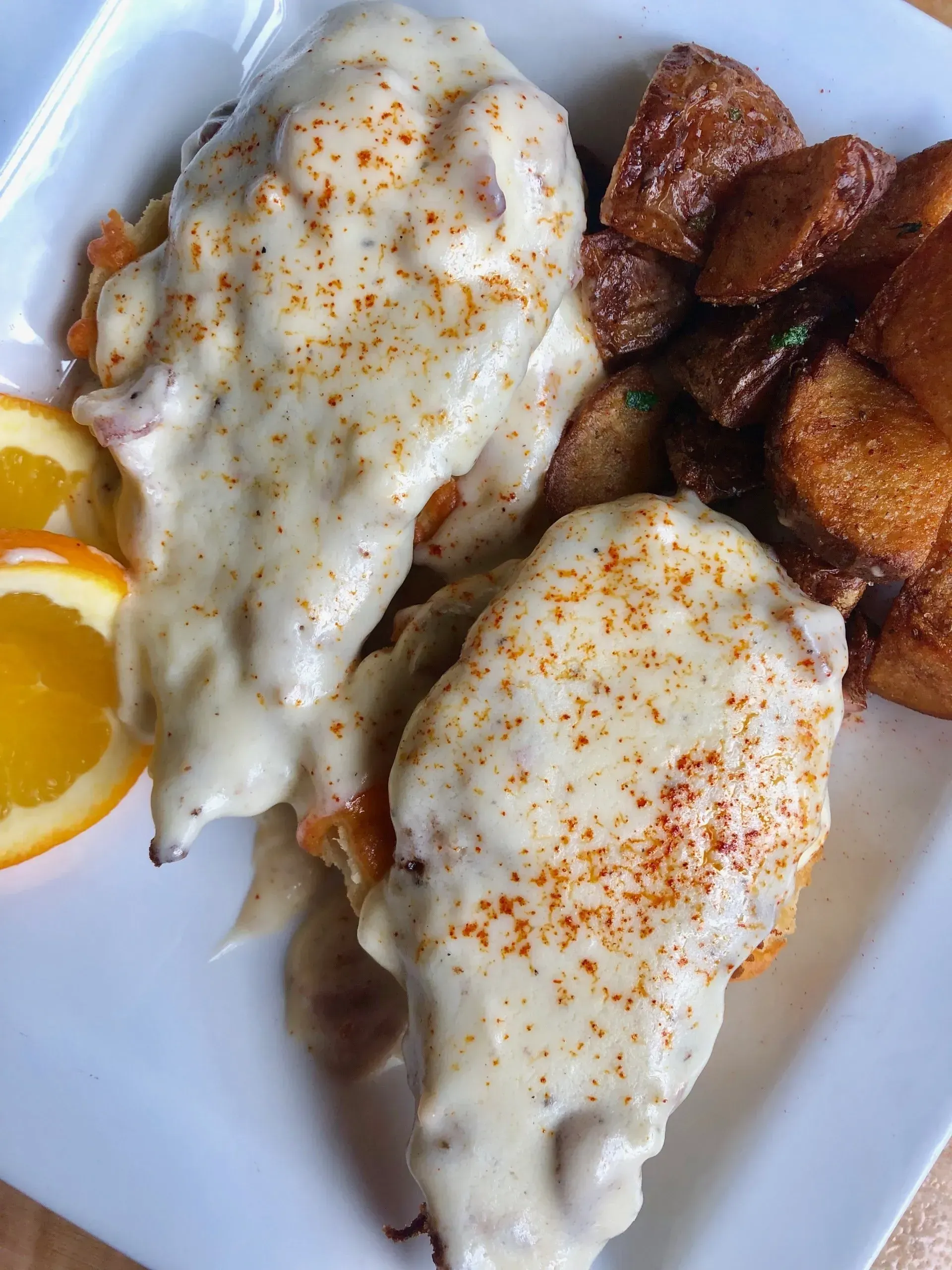 Plate of eggs smothered in white gravy with seasoned potatoes and orange slices on the side