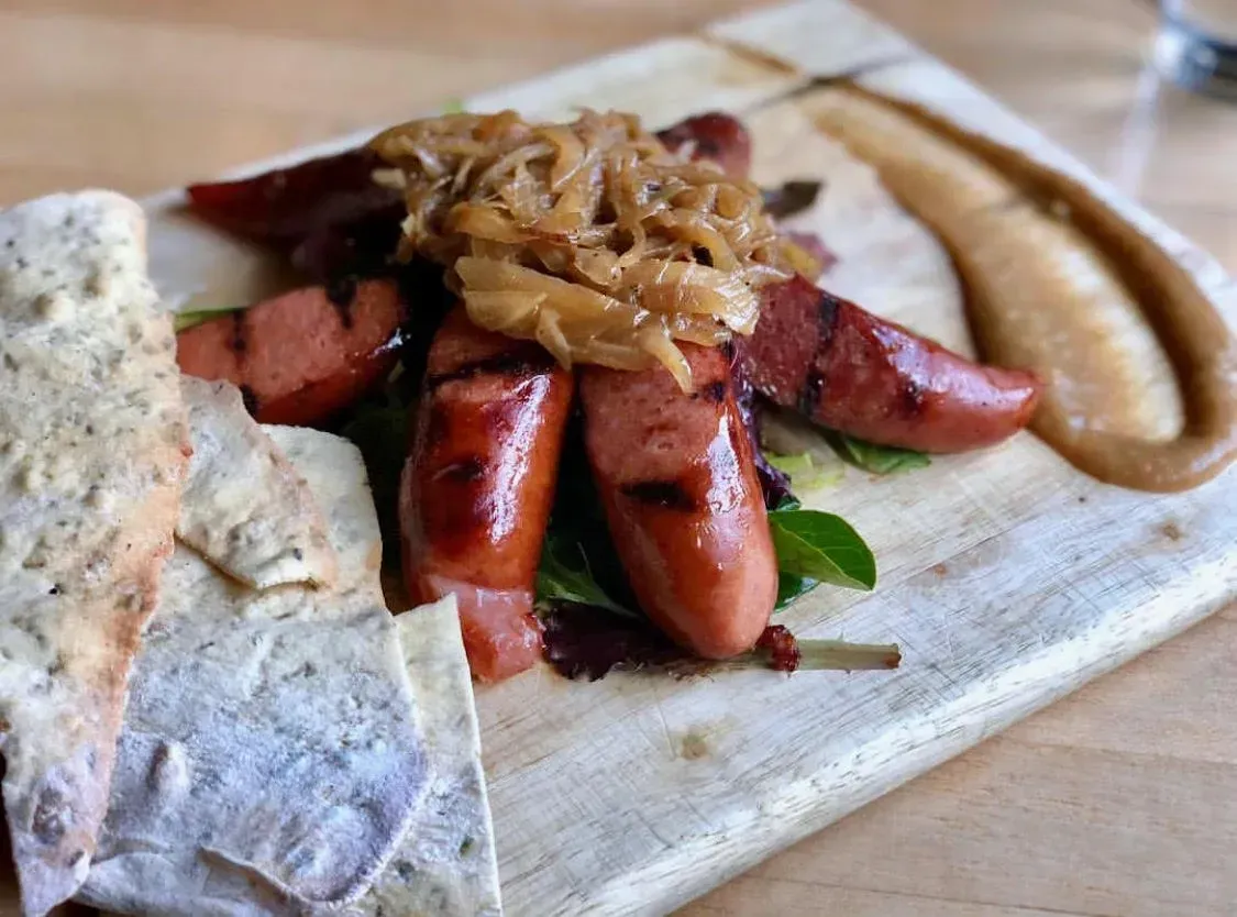 Plated sausage dish with caramelized onions, sauce, and bread on a wooden board