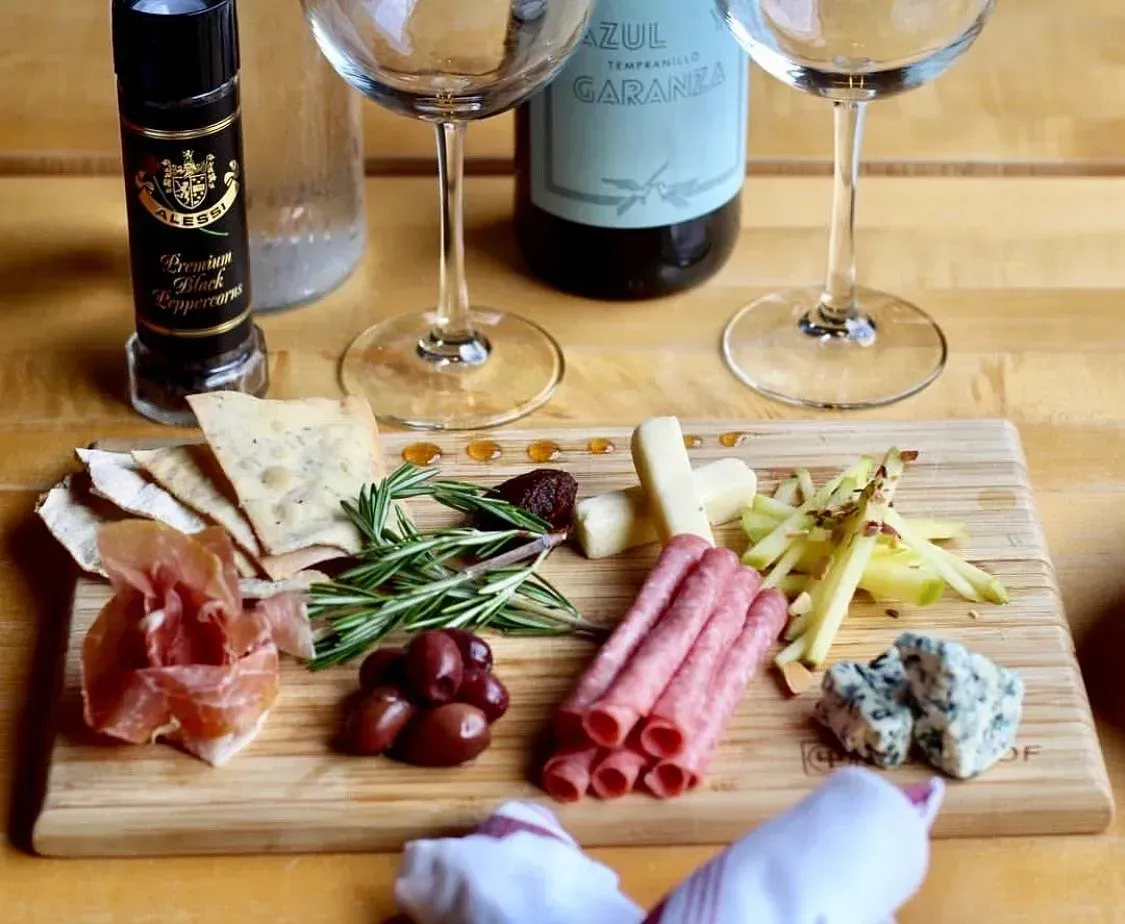 Wine and charcuterie board with cheese, grapes, crackers, ham, and bread on a table