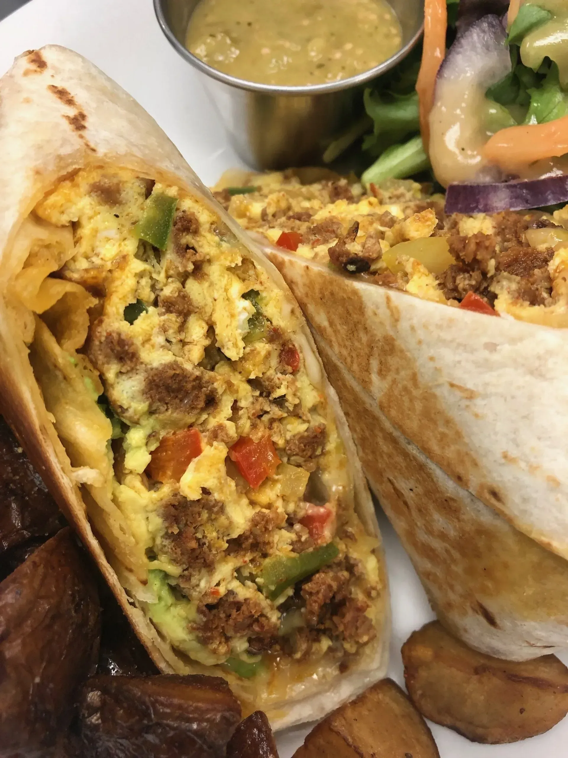 Two cut burritos on a plate with salsa and dipping sauce, showing rice, beans, and vegetables.