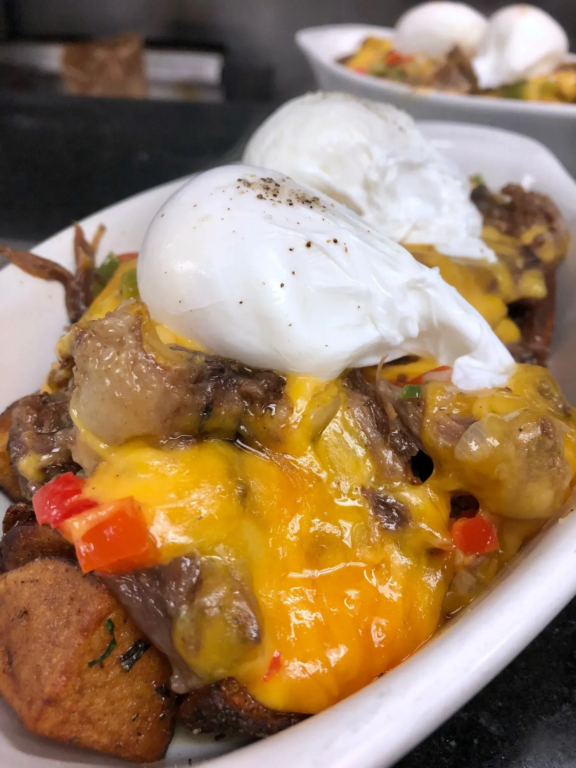 Poutine topped with poached eggs on a white dish, with melted cheese, gravy, and diced peppers.