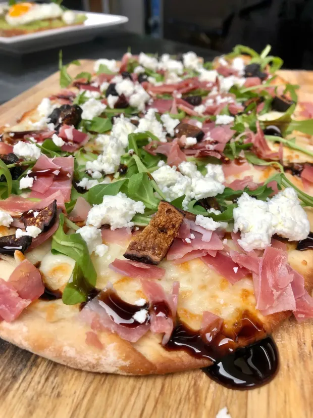 Gourmet flatbread pizza topped with arugula, prosciutto, cheese, and balsamic glaze on a wooden board