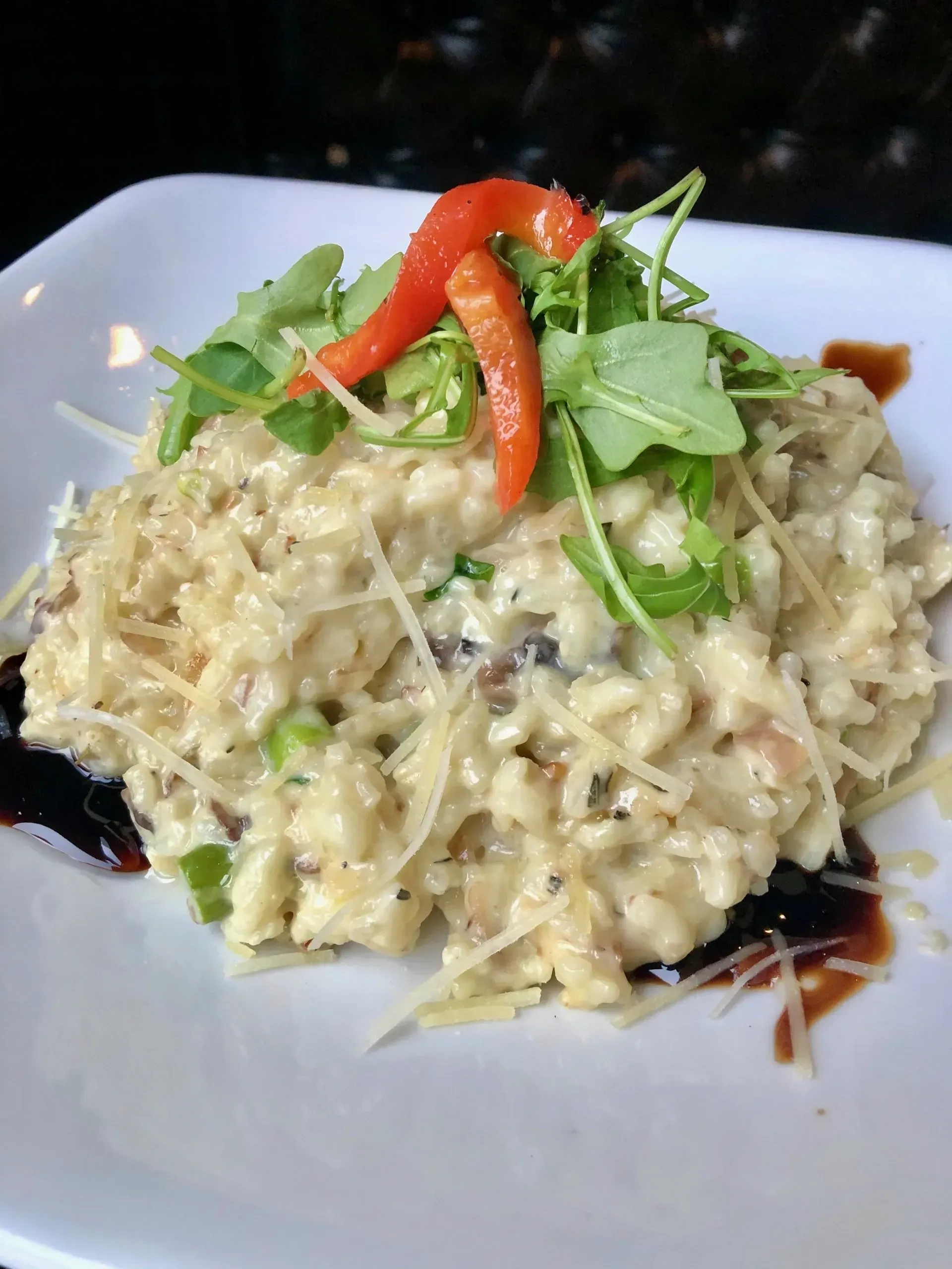 Creamy risotto topped with greens and red pepper on a white plate with balsamic drizzle