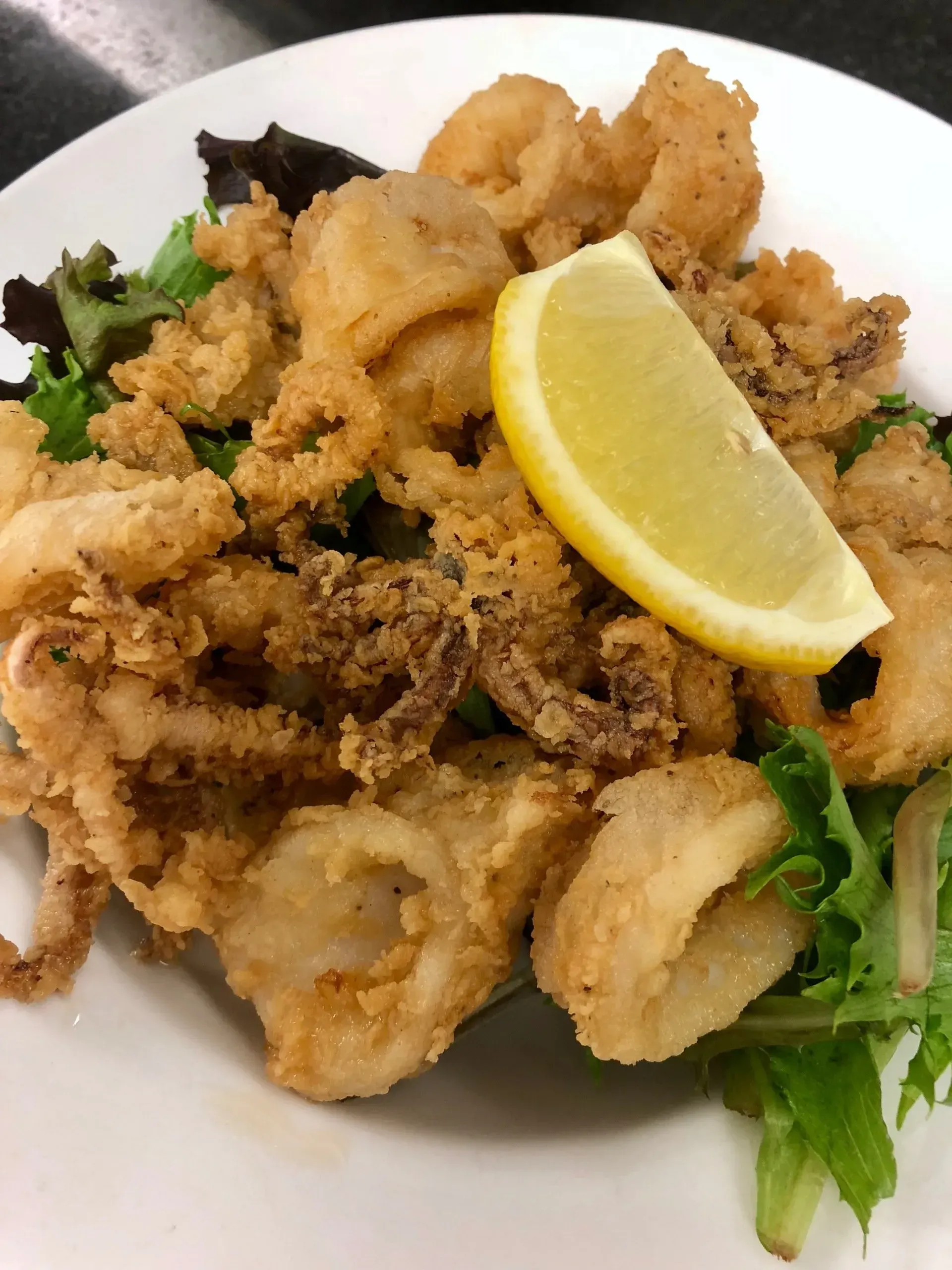 Fried calamari with a lemon wedge on a white plate, garnished with greens