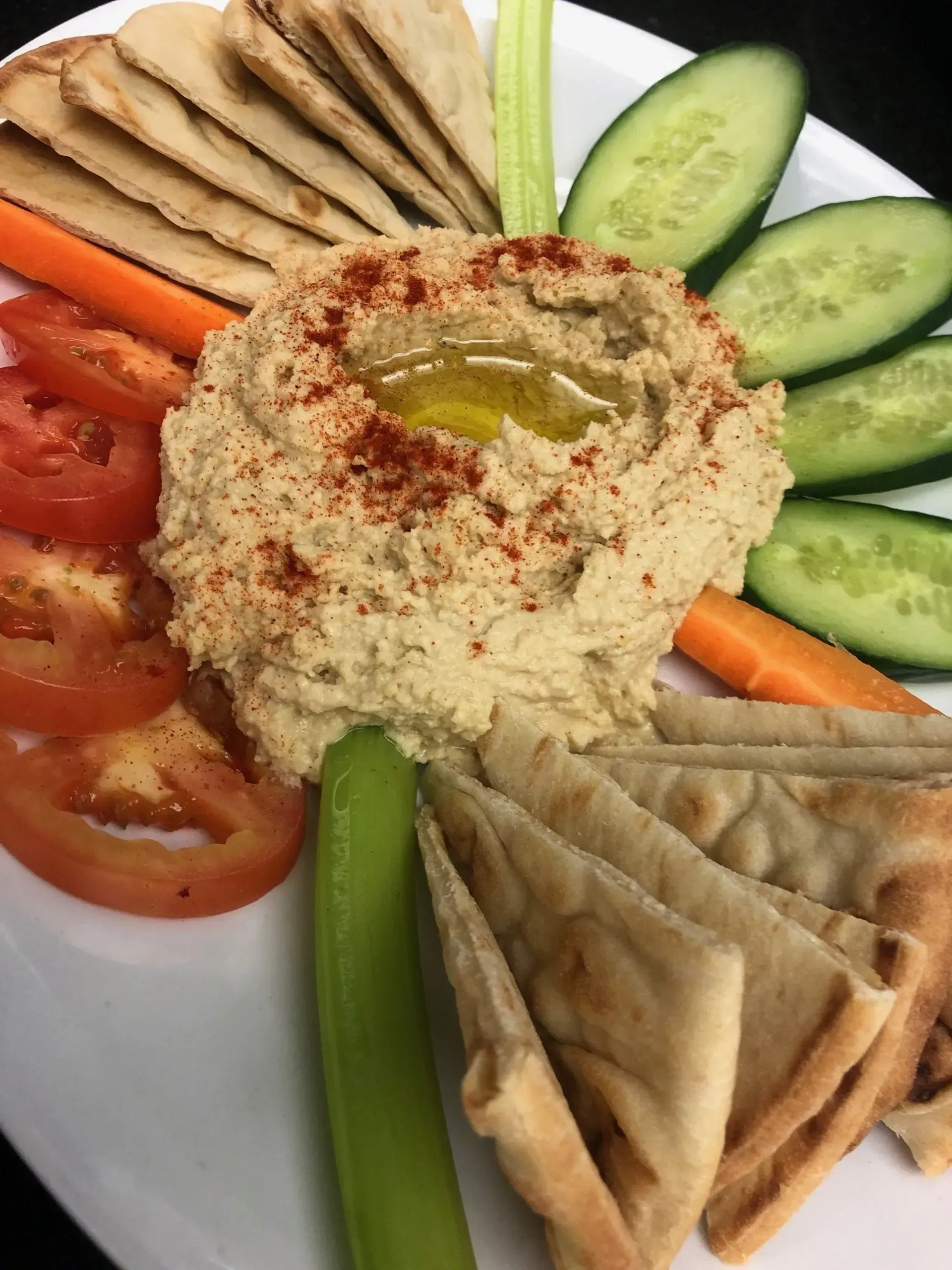 Hummus platter with pita wedges, cucumber, tomato, celery, and carrot sticks arranged on a plate