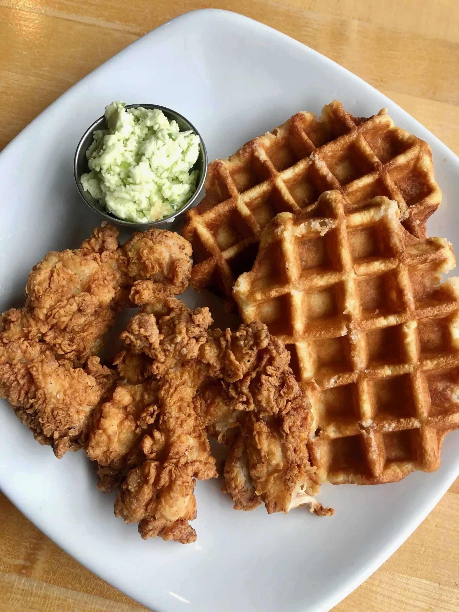 Fried chicken and waffles on a white plate with a small cup of green sauce