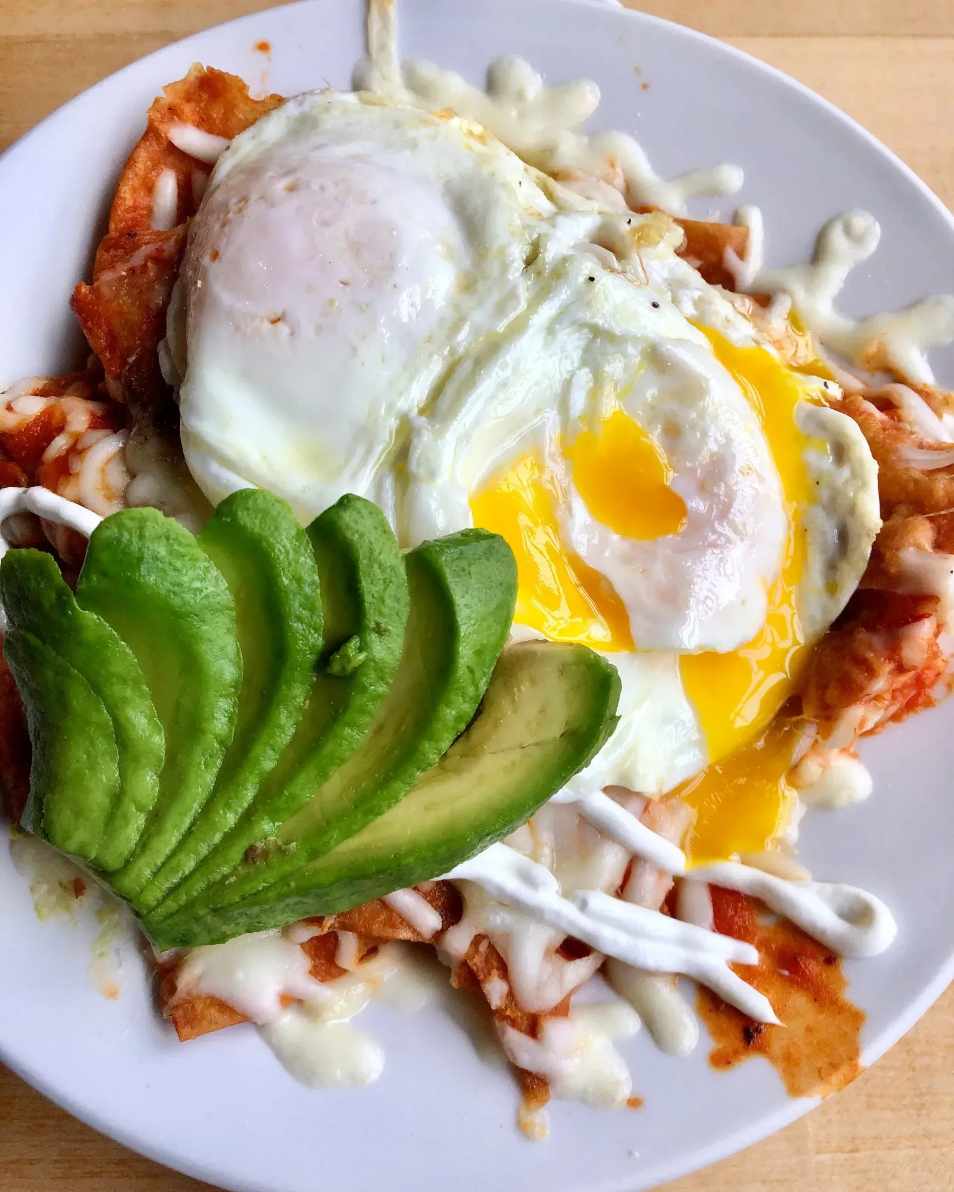Avocado slices and two fried eggs with sauce on a plate