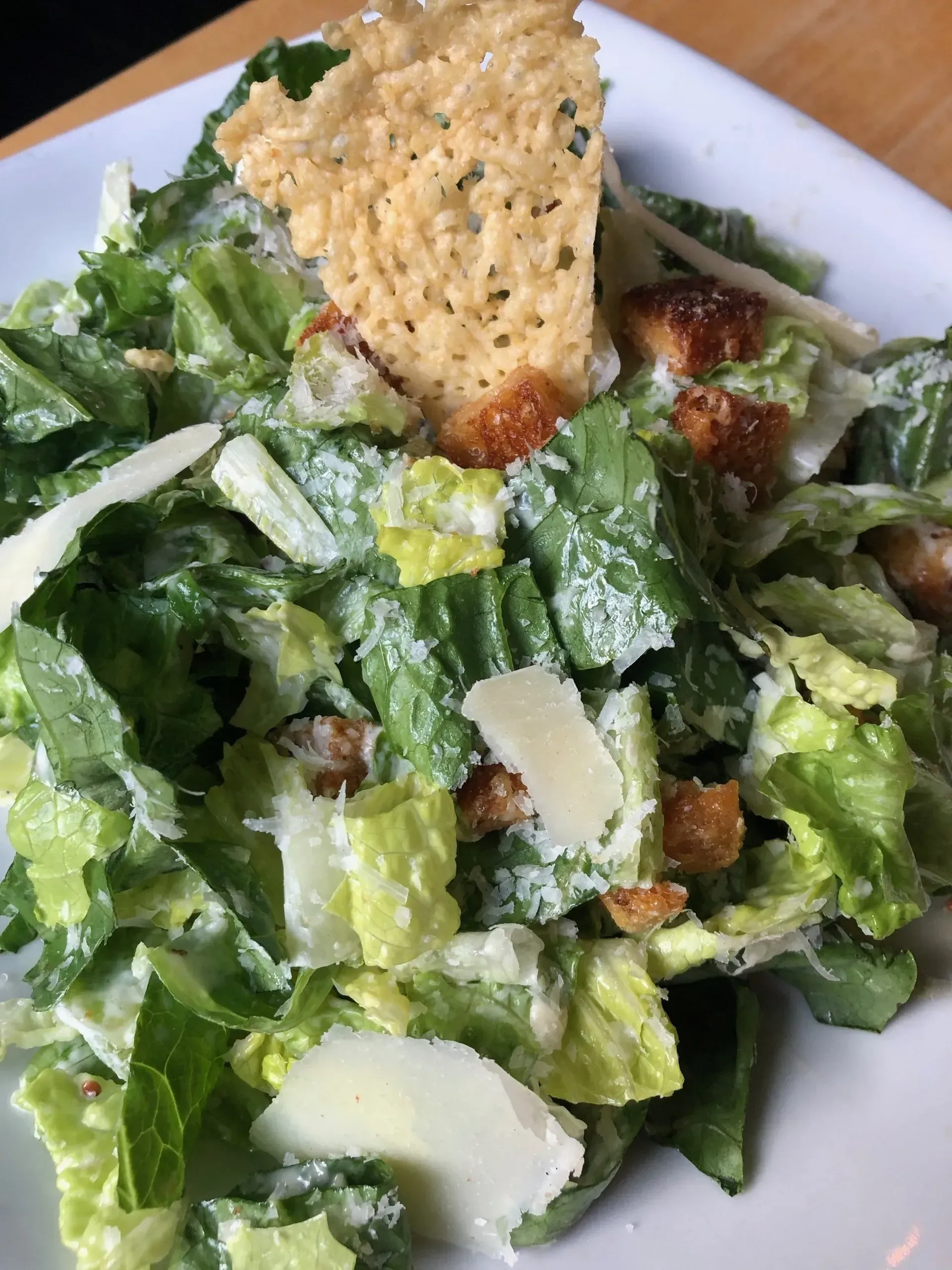 Caesar salad with romaine, parmesan shavings, croutons, and a crisp bread triangle on a white plate