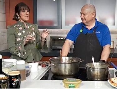 Two people cooking at a kitchen counter, talking beside pots and ingredients.
