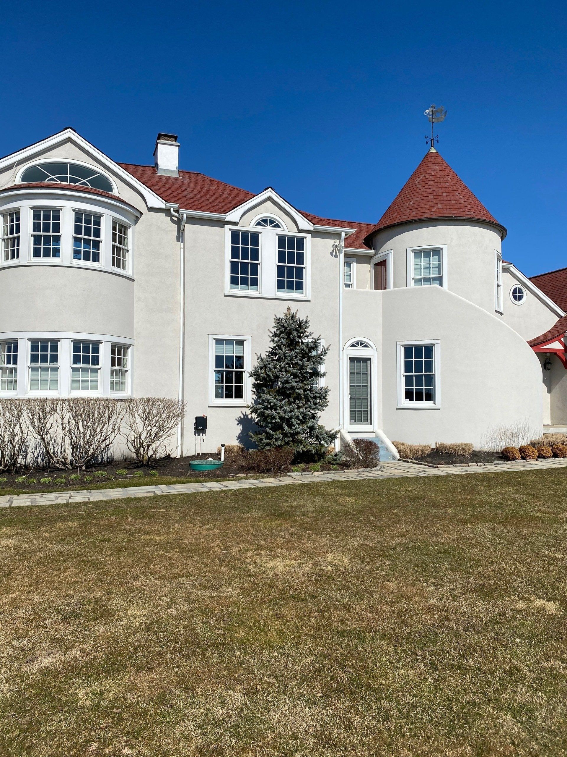 A large white house with a red roof is sitting on top of a lush green field.