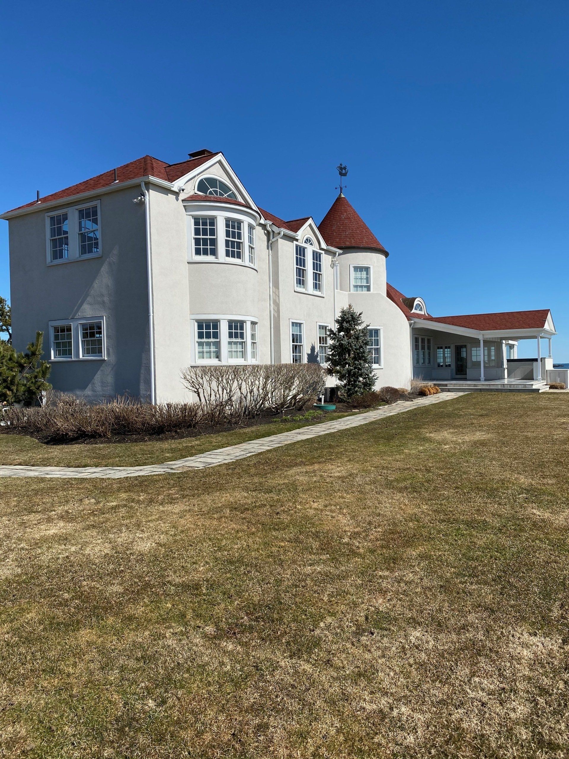 A large white house with a red roof is sitting on top of a grassy hill.