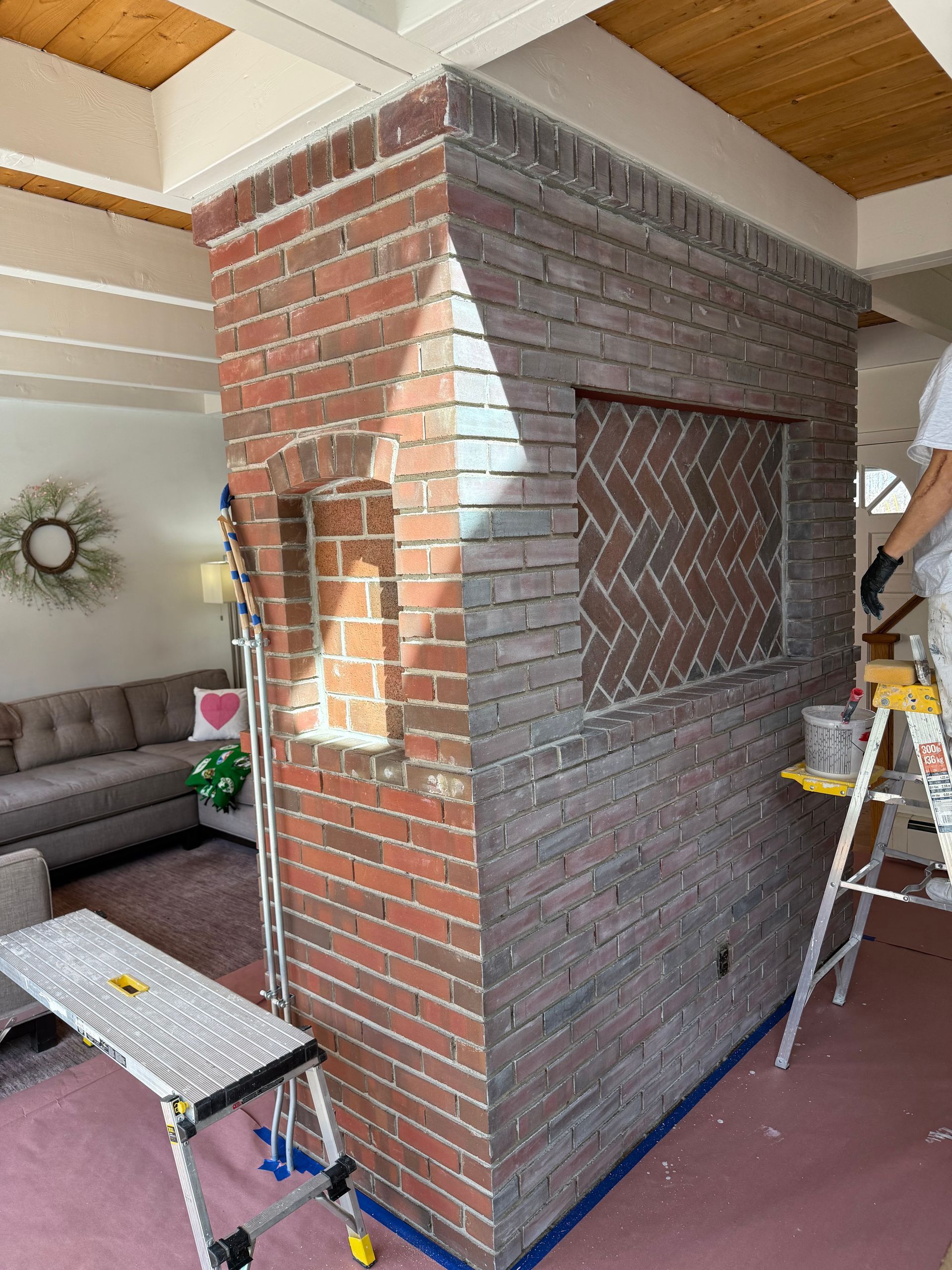 A man is painting a brick wall in a living room.