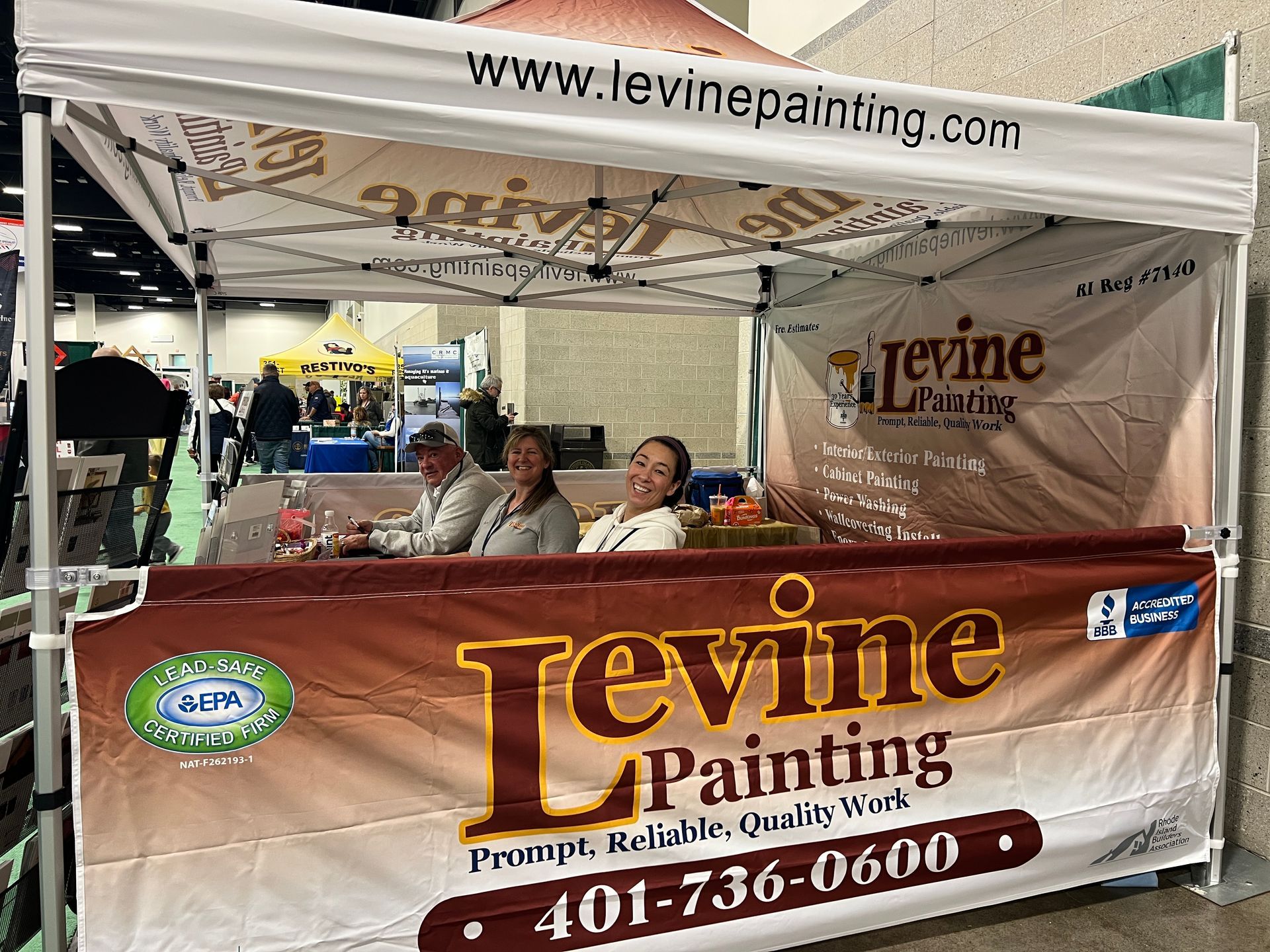 A group of people sitting under a tent that says levine painting