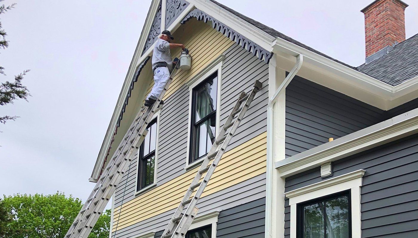 A man is painting the side of a house with a ladder.