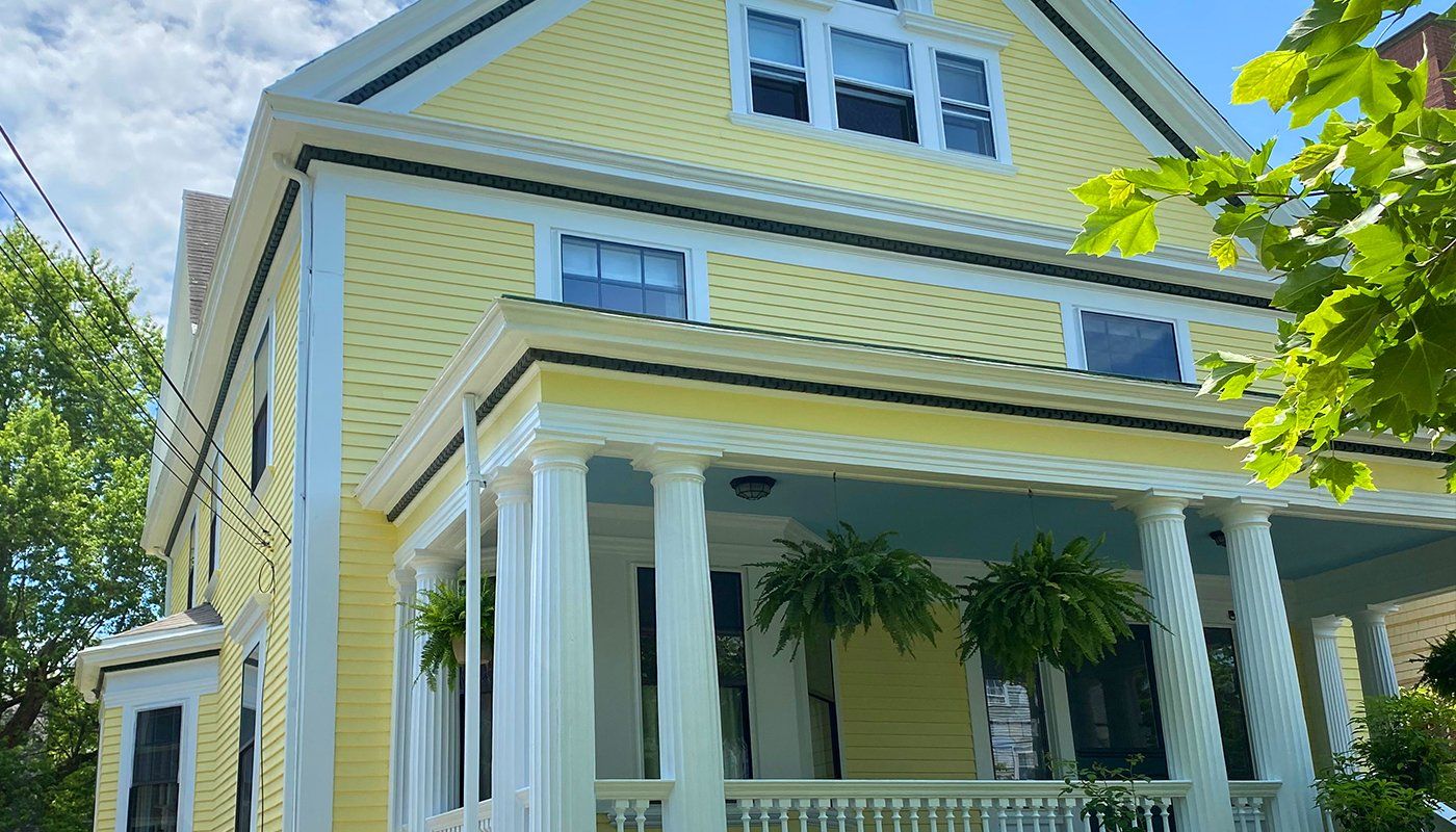 A yellow house with a large porch and a blue roof.