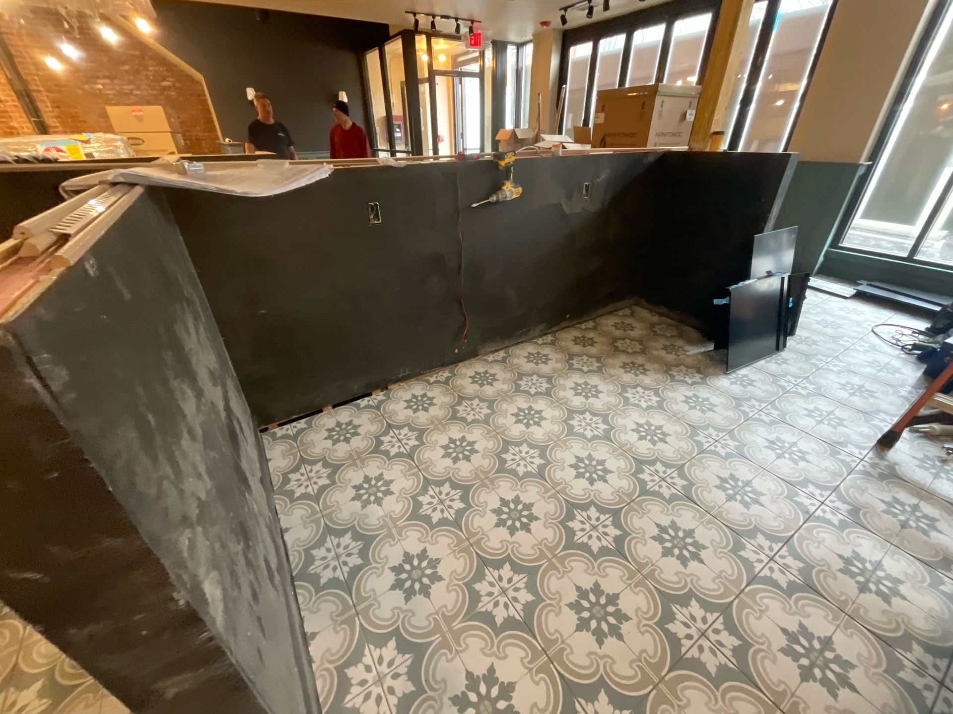 A tiled floor and partially built counter in a construction site, with two people visible in the background.