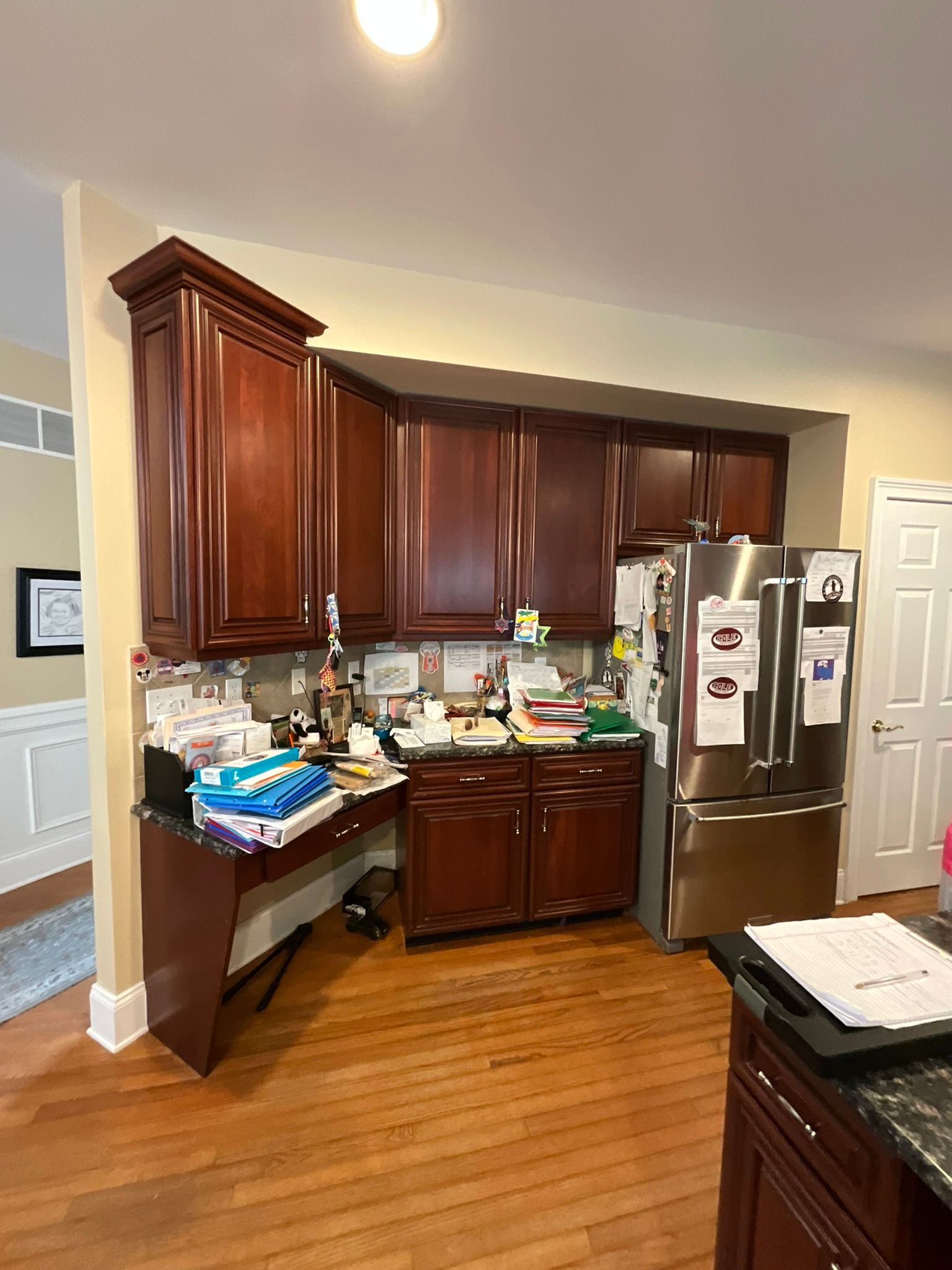 Kitchen with dark wood cabinets, stainless steel fridge, and cluttered countertop.