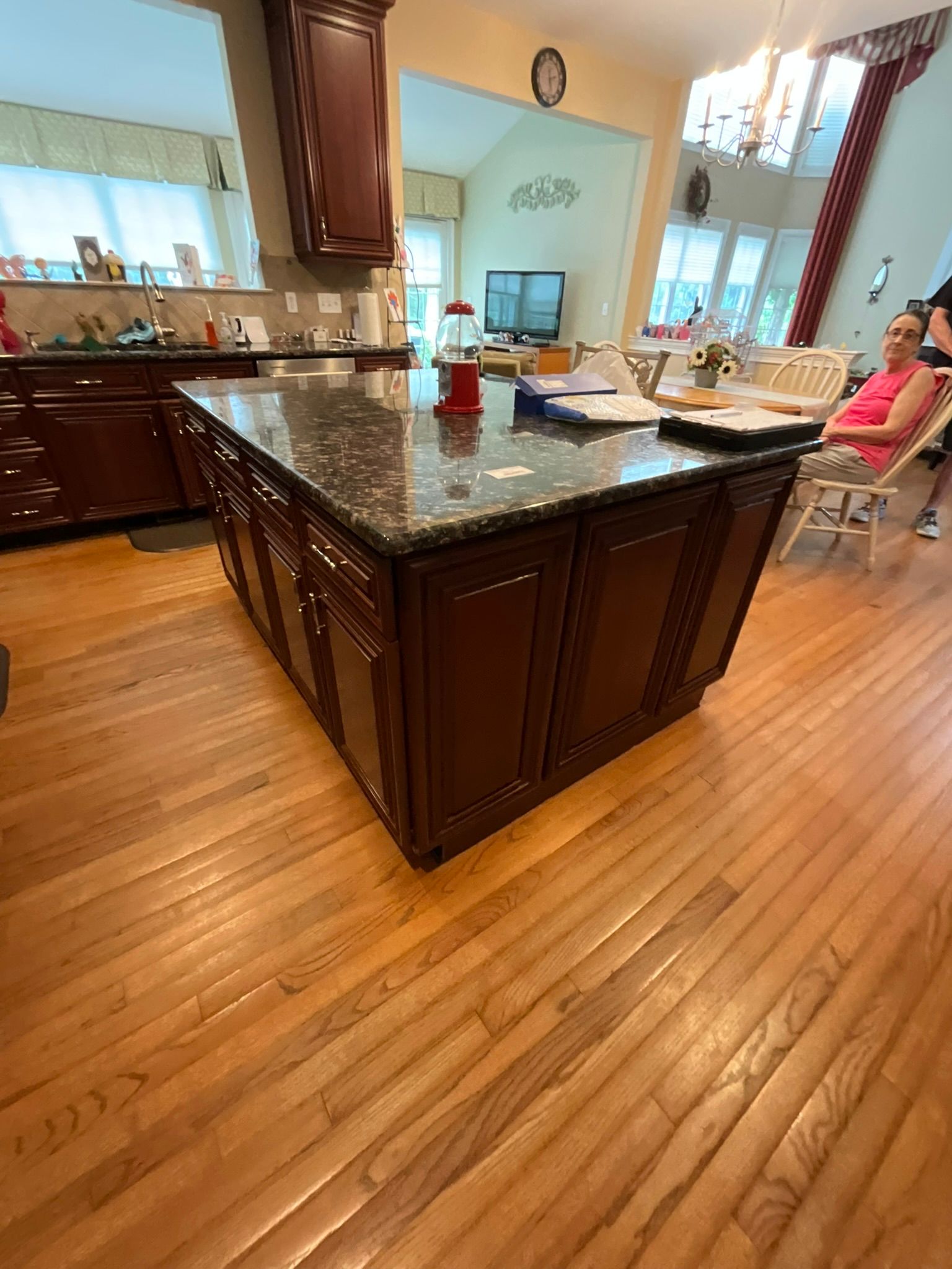 Kitchen with a dark wood island, granite countertop, and hardwood floors. A woman sits nearby.