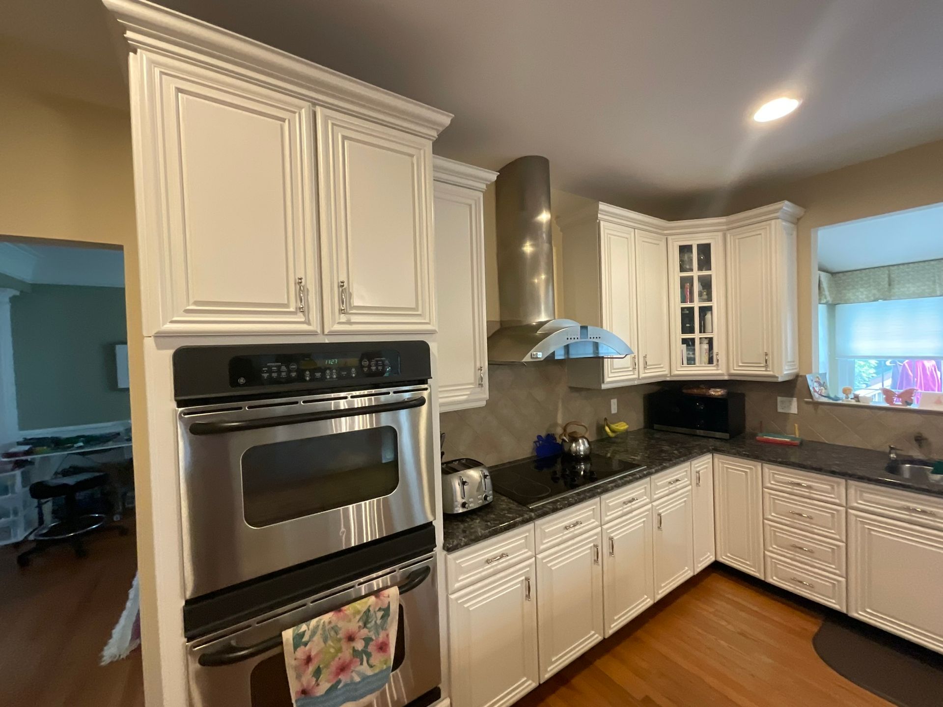 White kitchen with stainless steel appliances, black countertop, and wood floors.