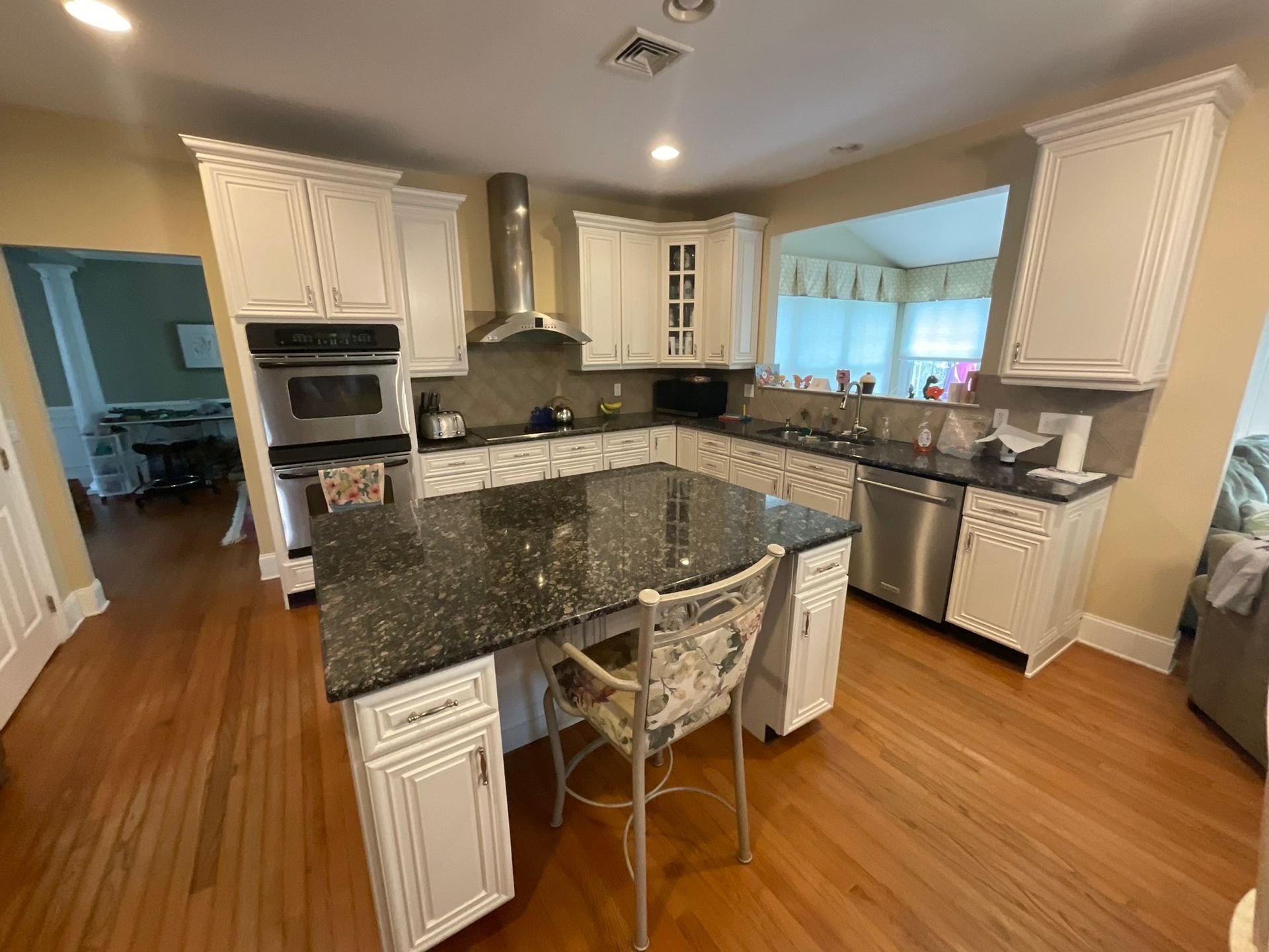 White kitchen with granite countertops, stainless steel appliances, and hardwood floors.