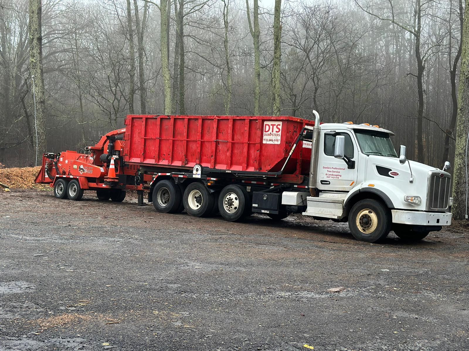 A truck with a red dumpster attached to it is parked in a parking lot.