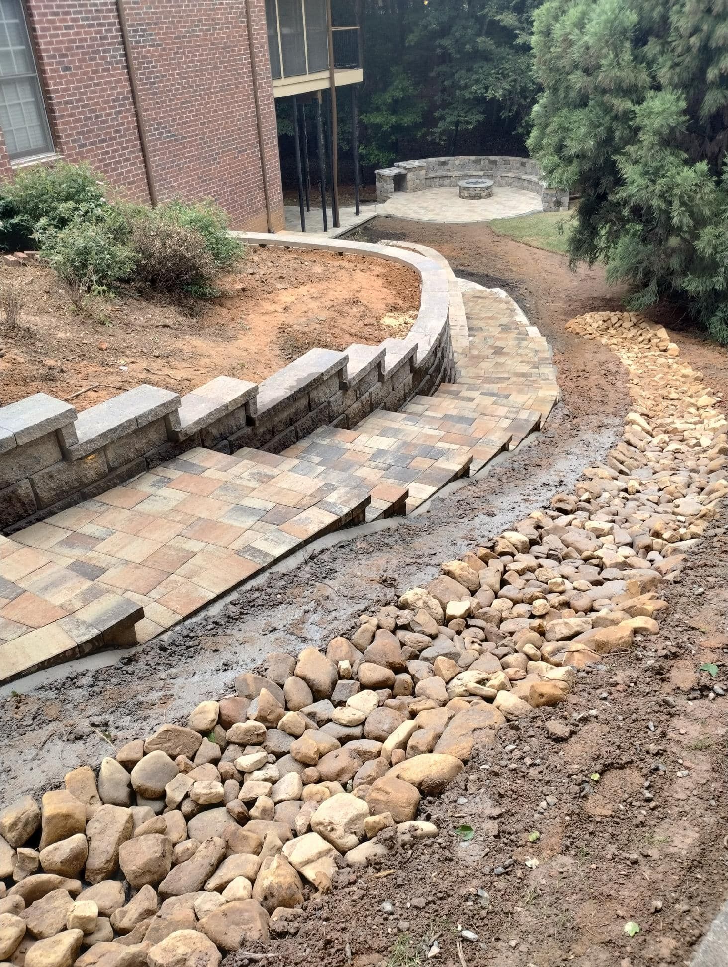 A stone walkway is being built in a backyard next to a brick building.