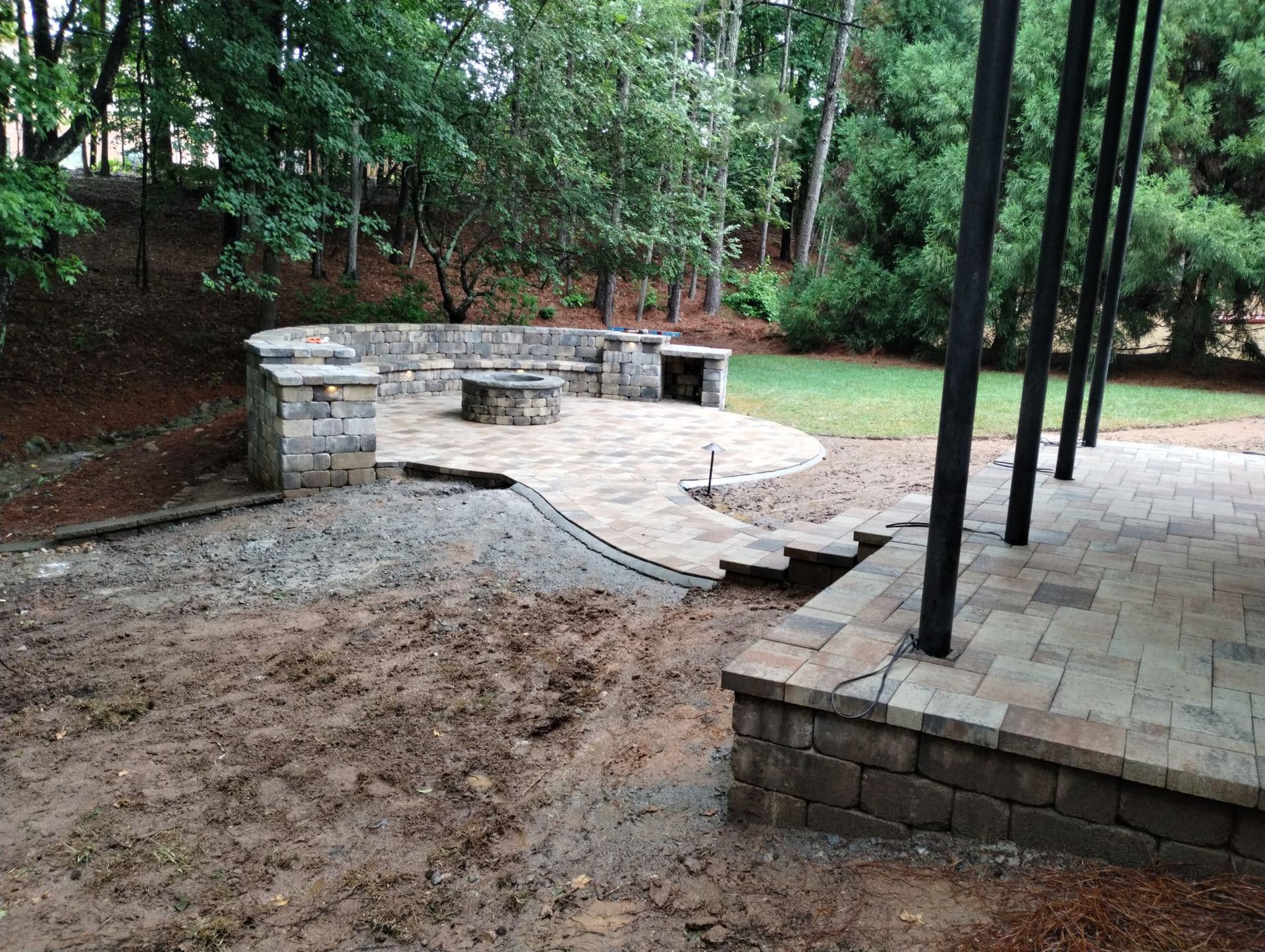 A backyard with a patio and a fire pit surrounded by trees.