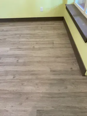 Wood-look flooring in a room with yellow walls and a brown baseboard.