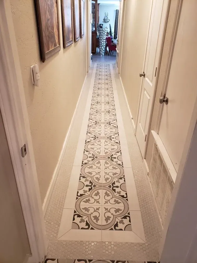 Narrow hallway with patterned tile floor, framed art, and closed doors.