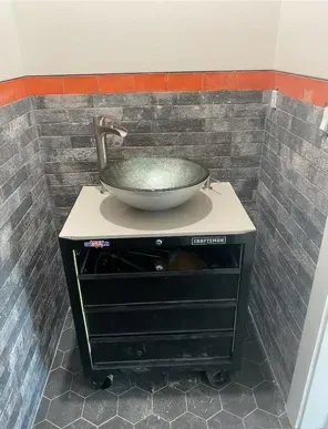 Vanity sink in a small bathroom, mounted on a black tool chest. Gray and orange tile, chrome faucet, and glass bowl.