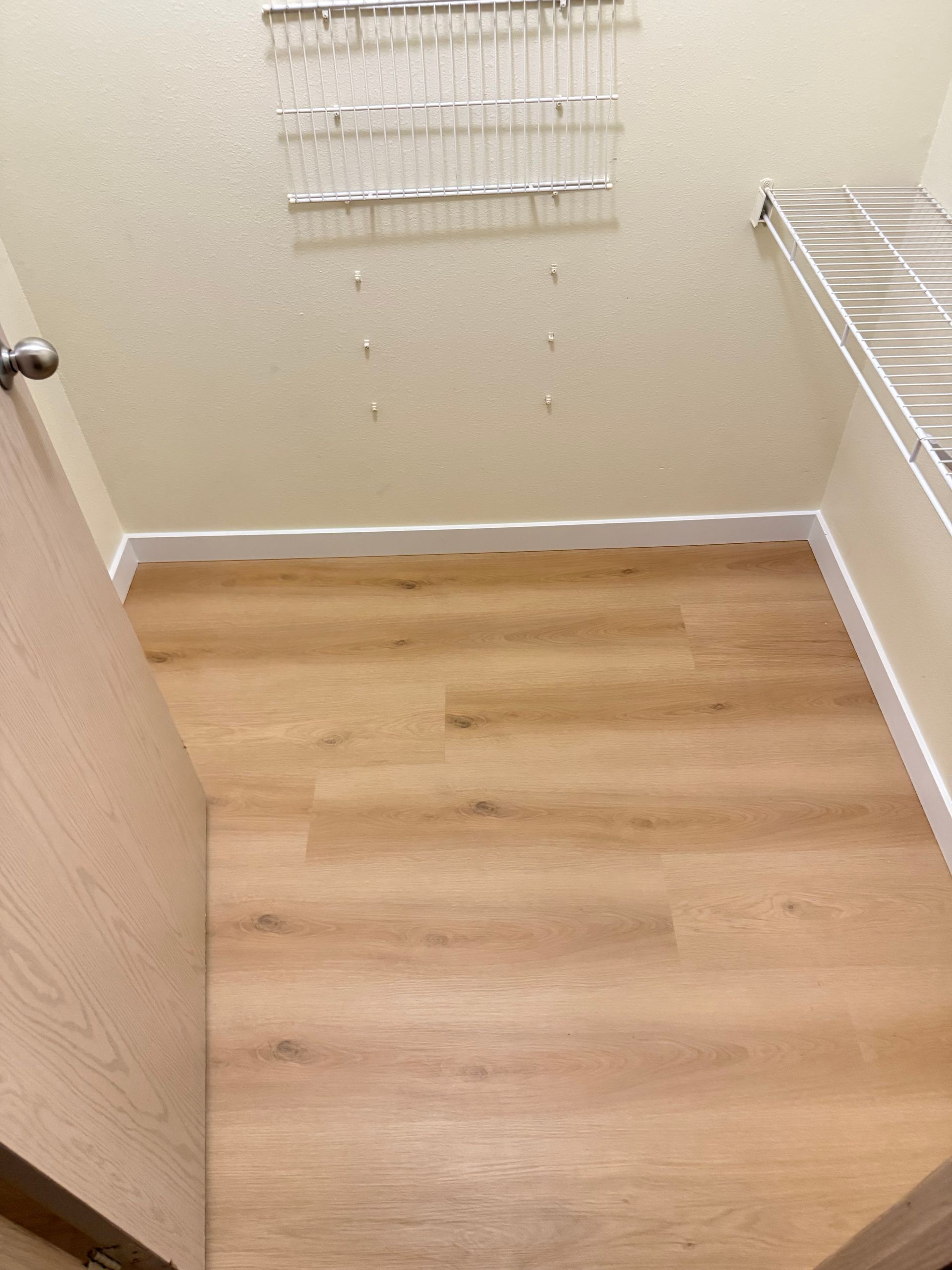 Laundry room with wood-look flooring, beige walls, and white trim. A wire shelf hangs on the wall.